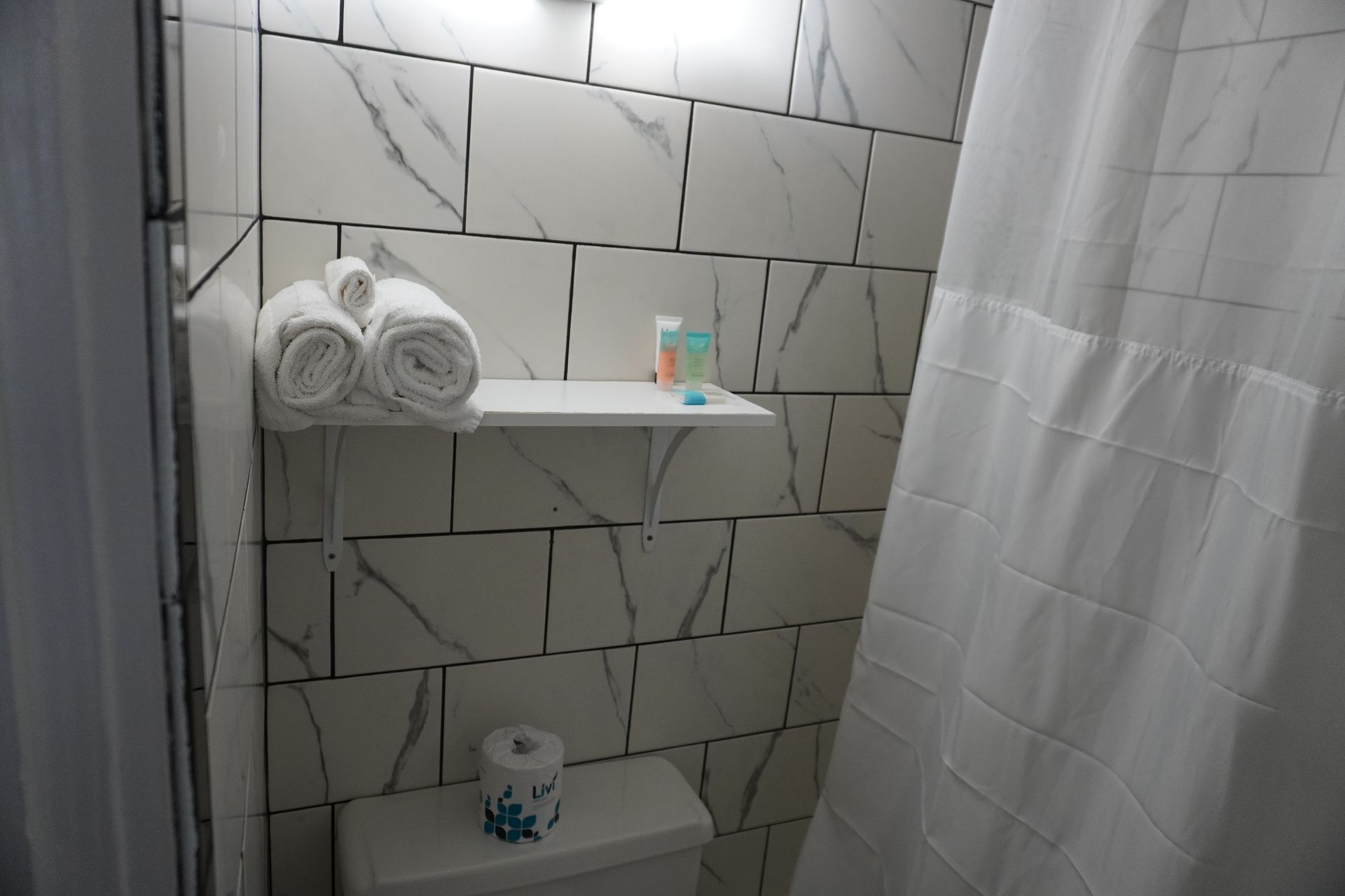 A bathroom with a toilet , shower curtain and a shelf with towels on it.