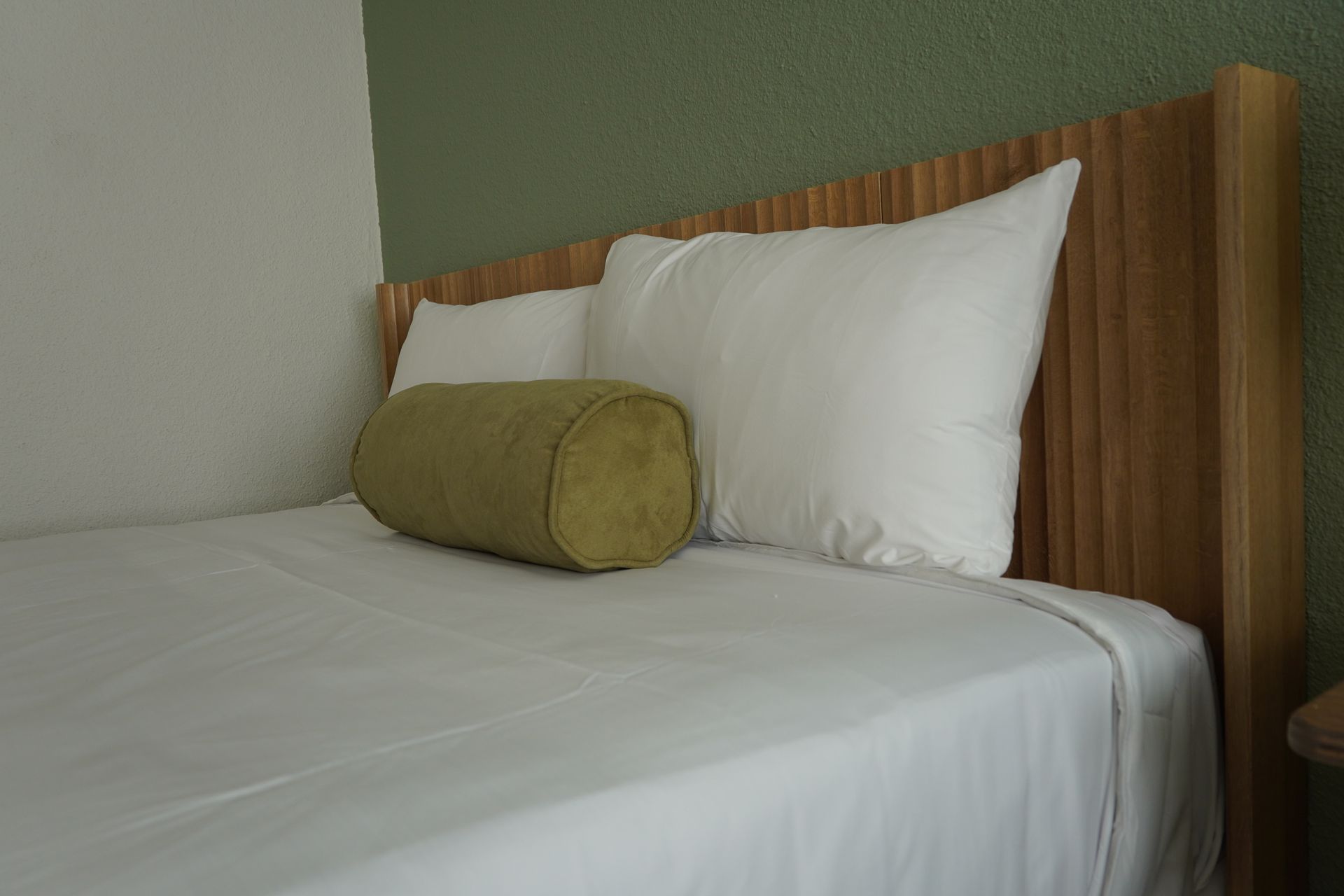 A bed with white sheets and a green pillow on it.