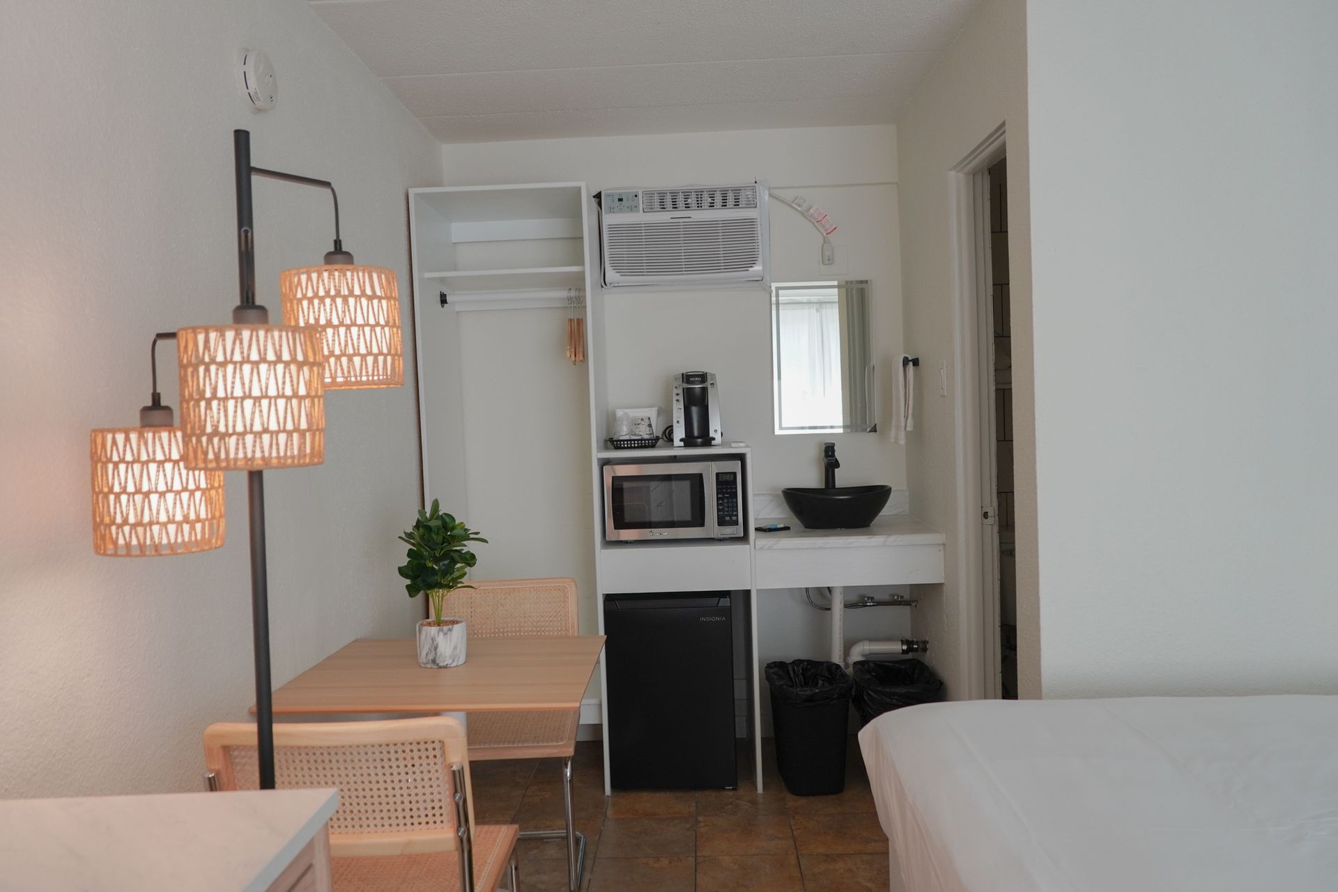 A small room with a table , chairs , microwave , sink and mirror.
