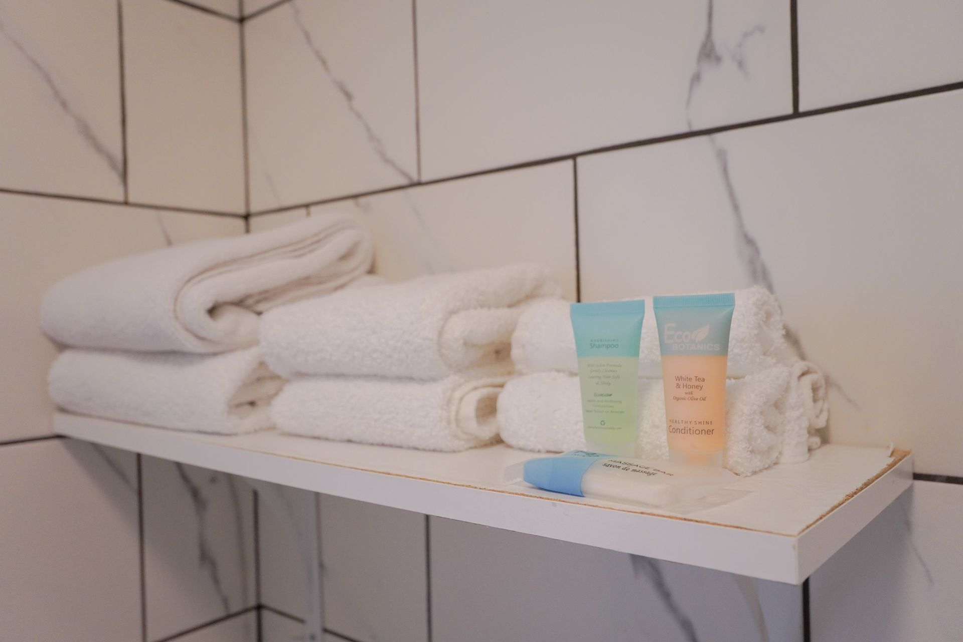 A bathroom shelf with towels , soap , and lotion on it.