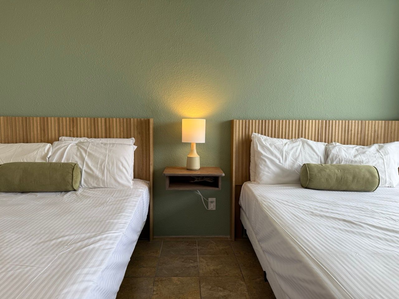 A hotel room with two beds and a lamp.
