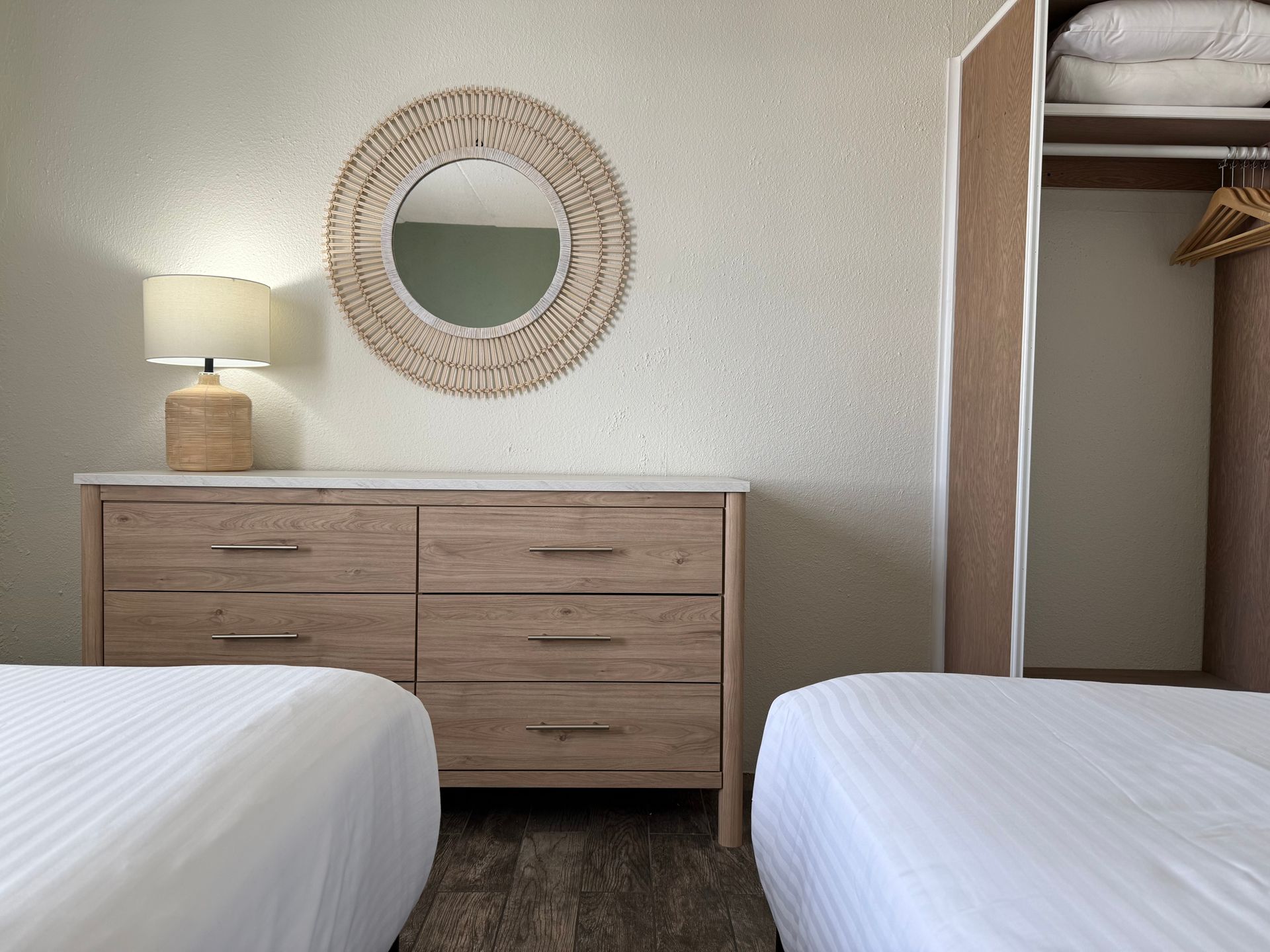 A bedroom with two beds , a dresser , a lamp and a mirror.
