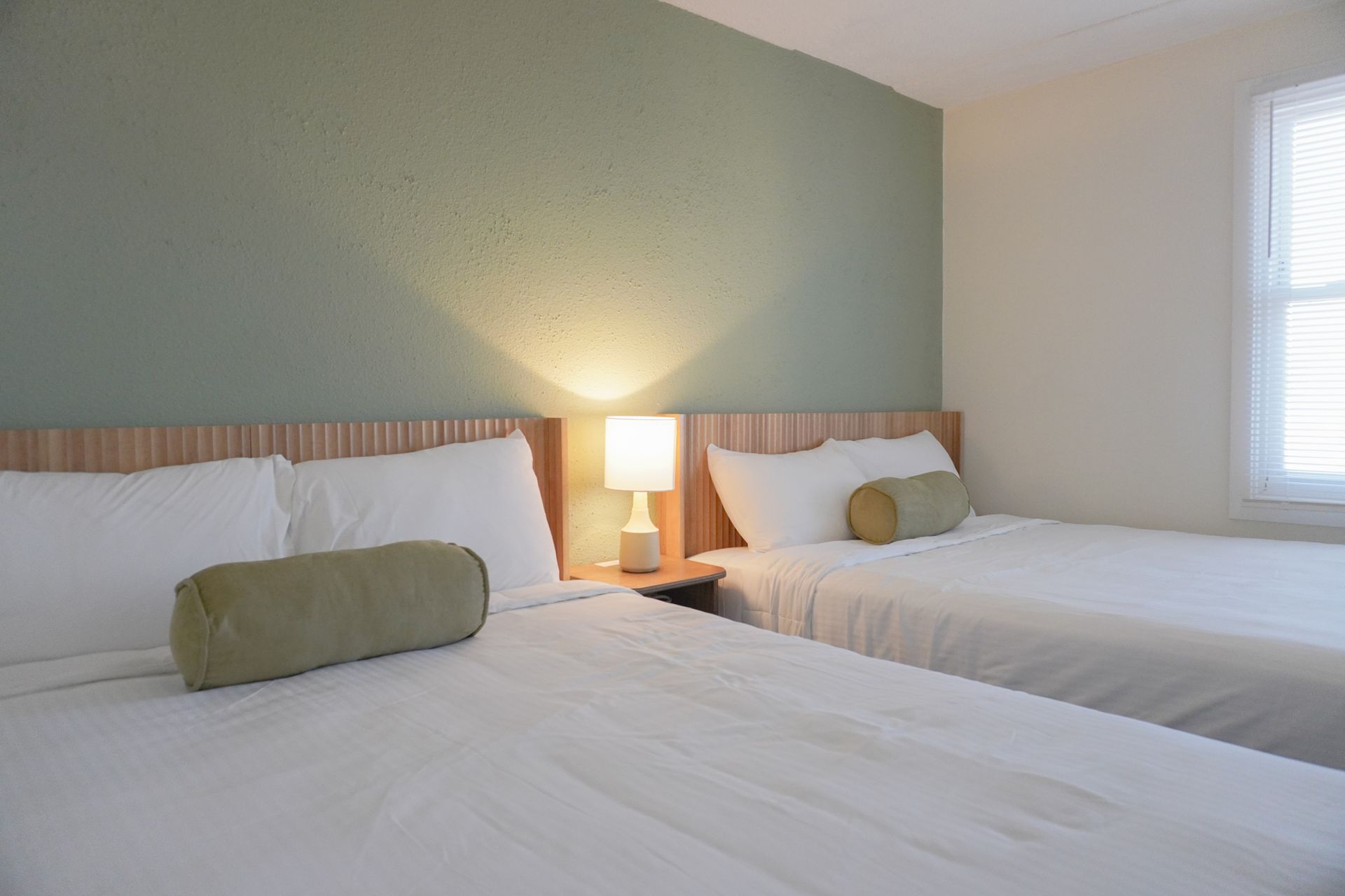 A hotel room with two beds , a lamp and a window.