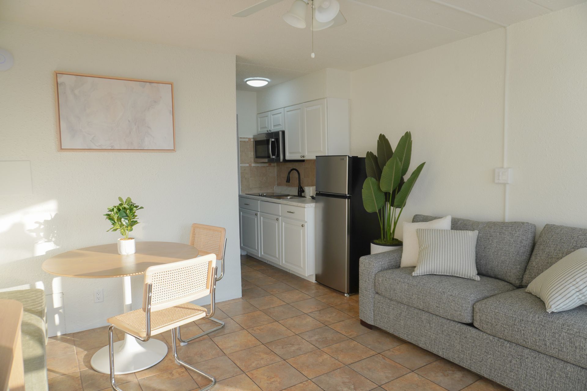 A living room with a couch , table , chairs and a refrigerator.