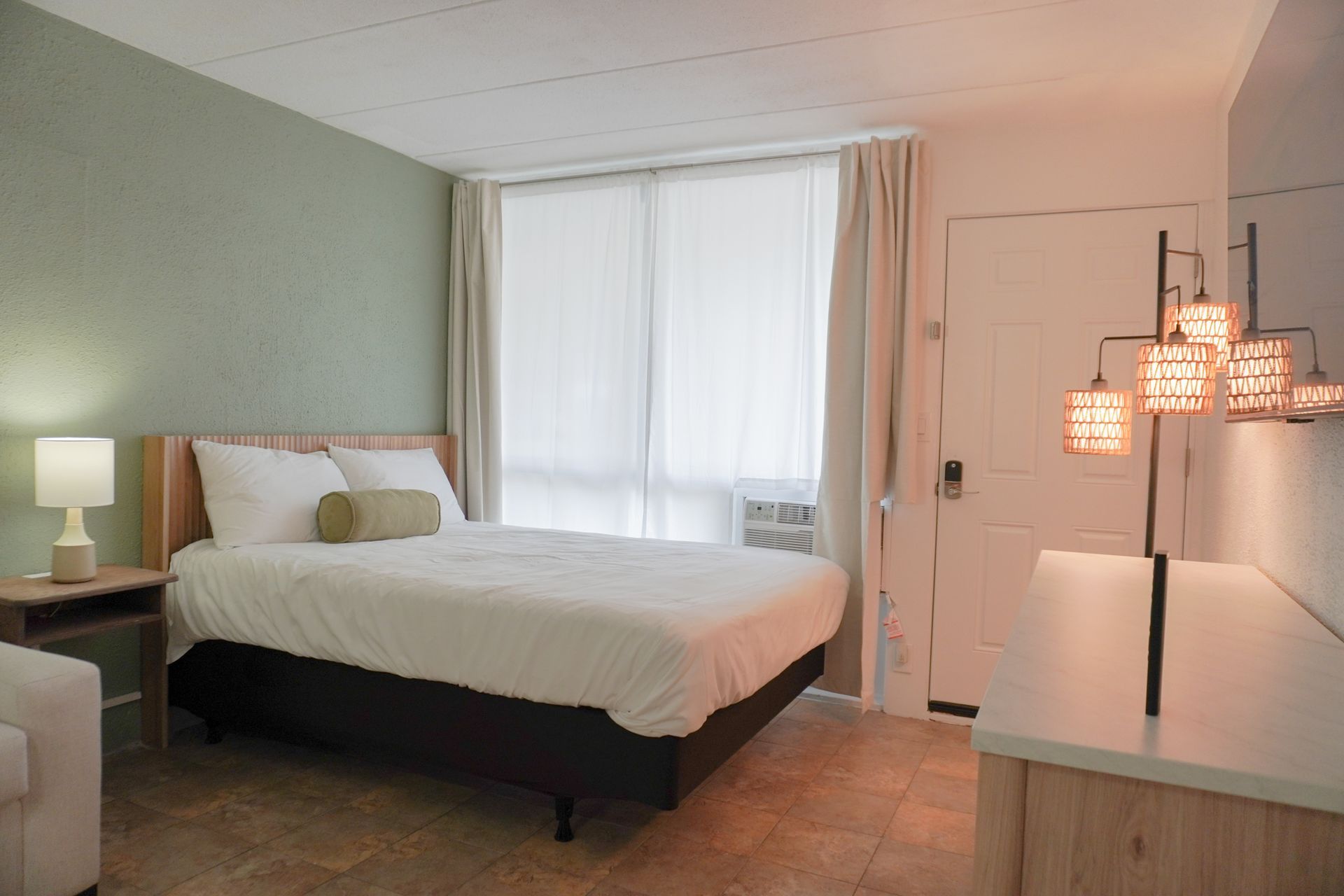 A hotel room with a bed , dresser , chair and window.