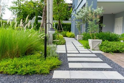Modern garden path with stepping stones, tall grasses, and a house beside a gravel courtyard