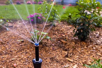 Garden sprinkler spraying water over mulch and flowers in a landscaped yard