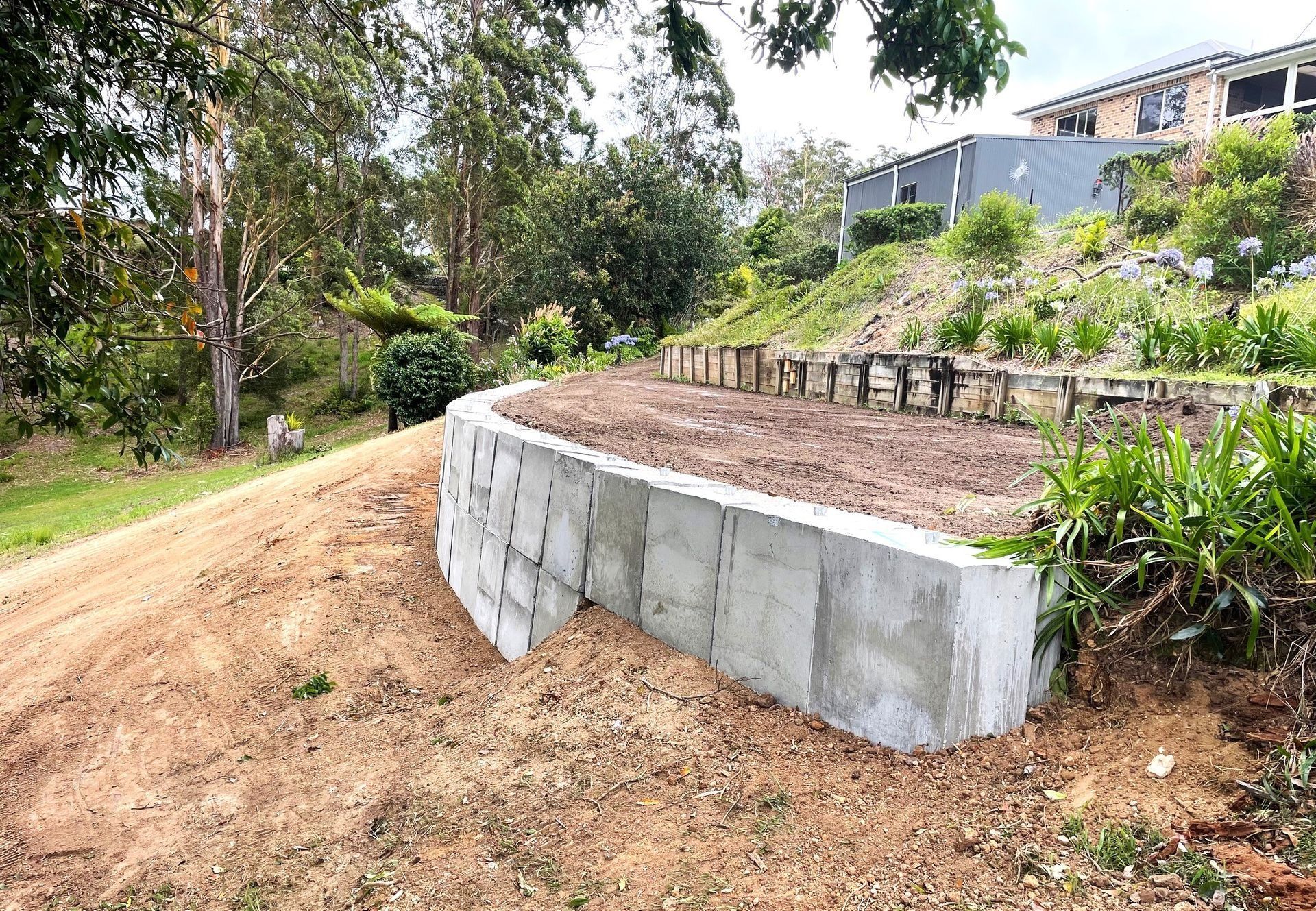Concrete Retaining Wall on a Hillside With Freshly Graded Dirt — Blue Dog Earthmoving Landscape Supplies in Newee Creek, NSW