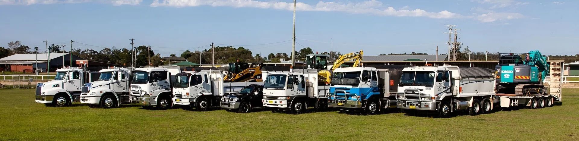 A Line of Trucks Parked on a Grassy Field — Blue Dog Earthmoving Landscape Supplies in Newee Creek, NSW