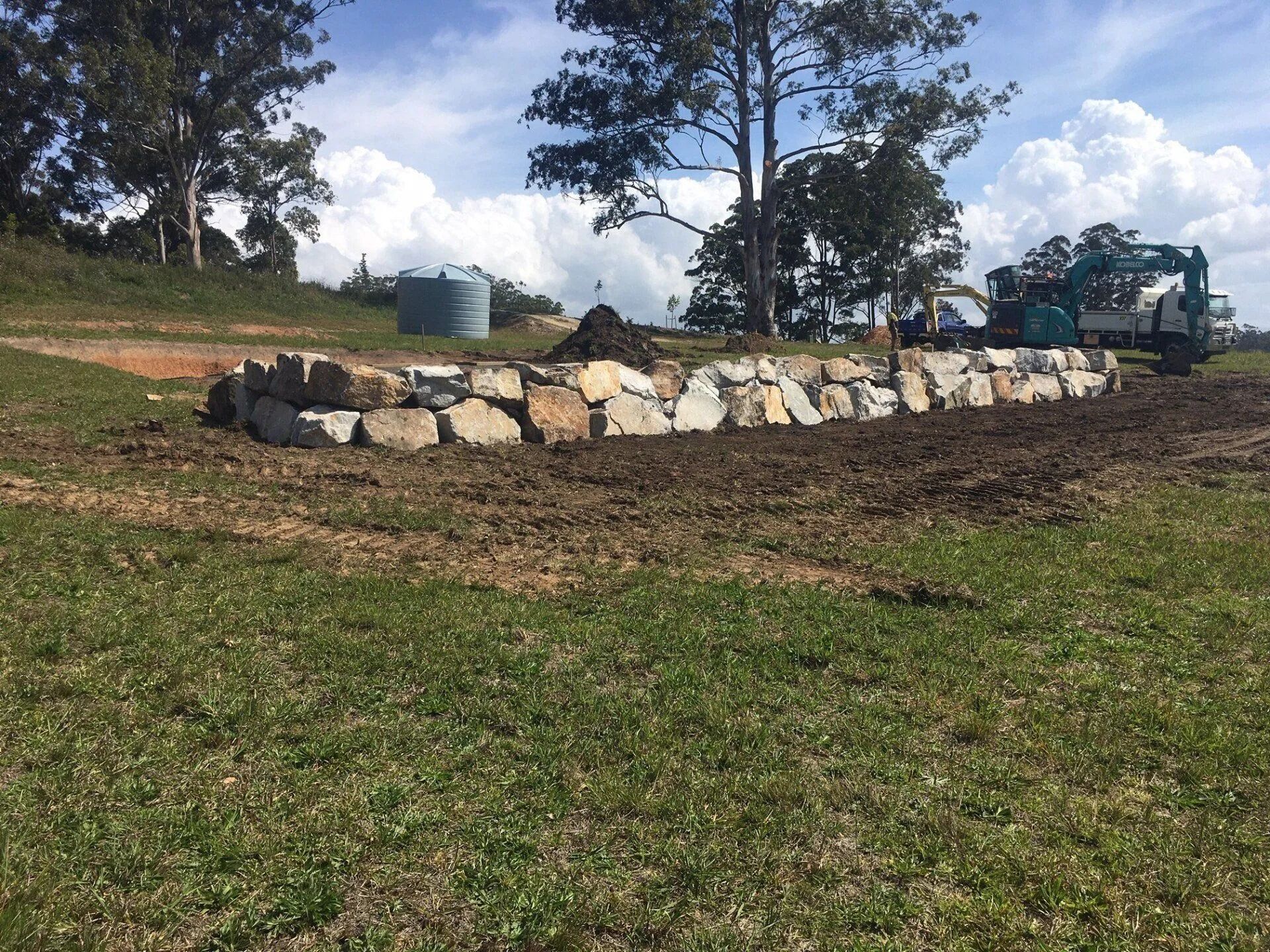 Stone Retaining Wall Under Construction on a Grassy Hill — Blue Dog Earthmoving Landscape Supplies in Newee Creek, NSW