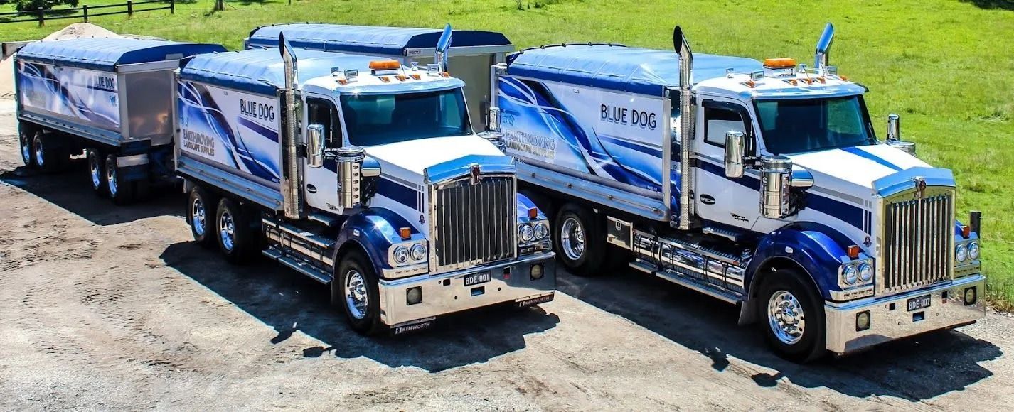 Two Blue and White Dump Trucks Parked on Gravel — Blue Dog Earthmoving Landscape Supplies in Bellingen, NSW