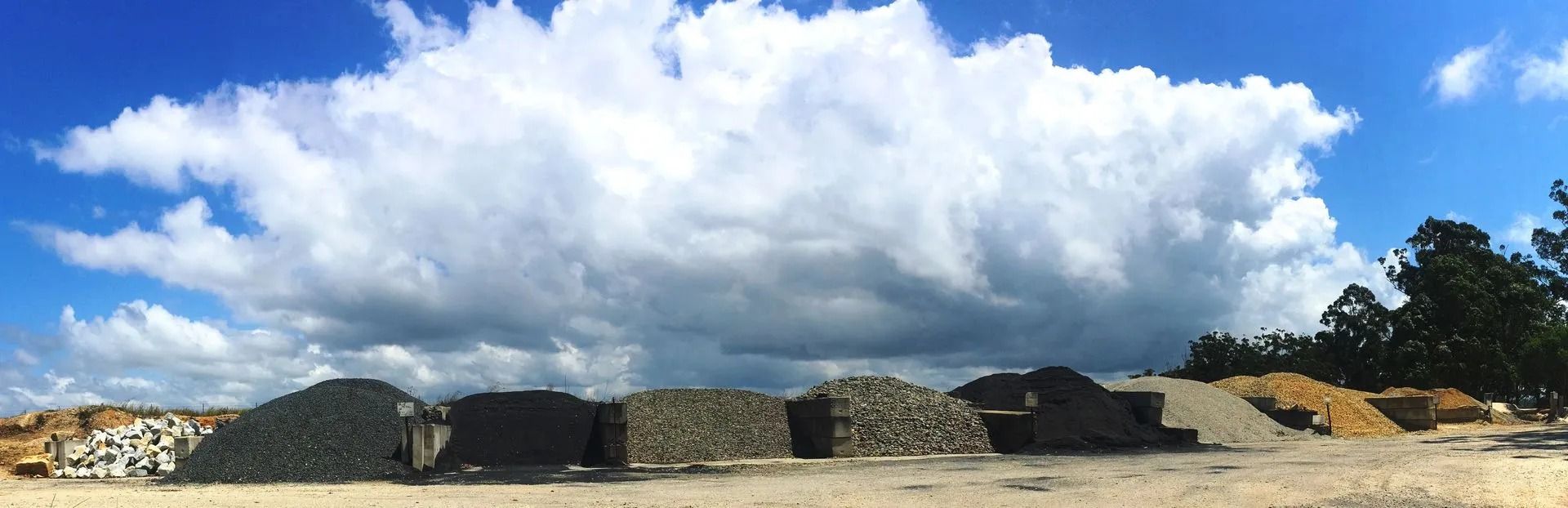 Piles of Gravel and Sand Sit in Front of a Blue Sky With Fluffy White Clouds — Blue Dog Earthmoving Landscape Supplies in Valla Beach, NSW