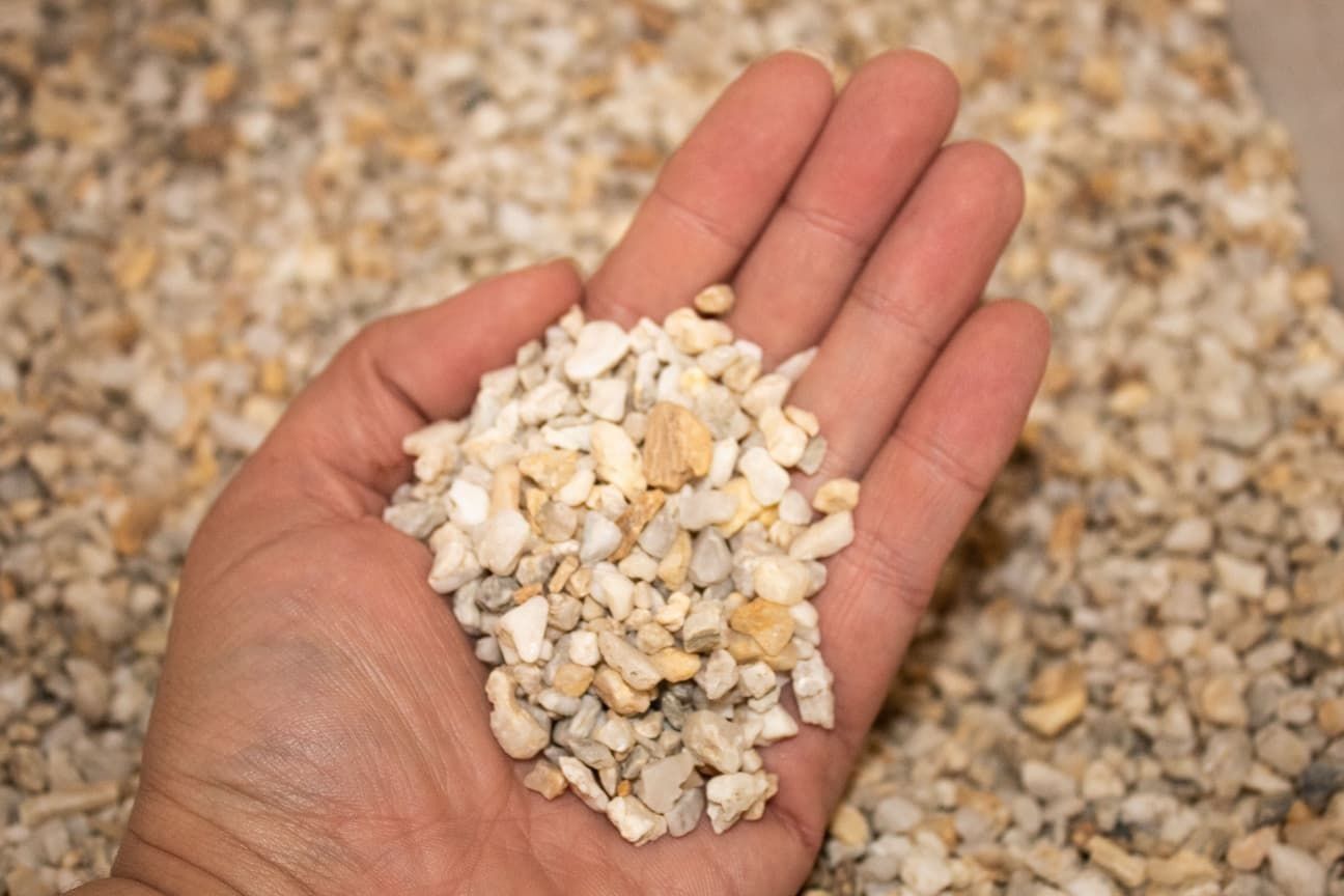 Hand Holding a Pile of Small, Light-coloured Gravel — Blue Dog Earthmoving Landscape Supplies in Valla Beach, NSW