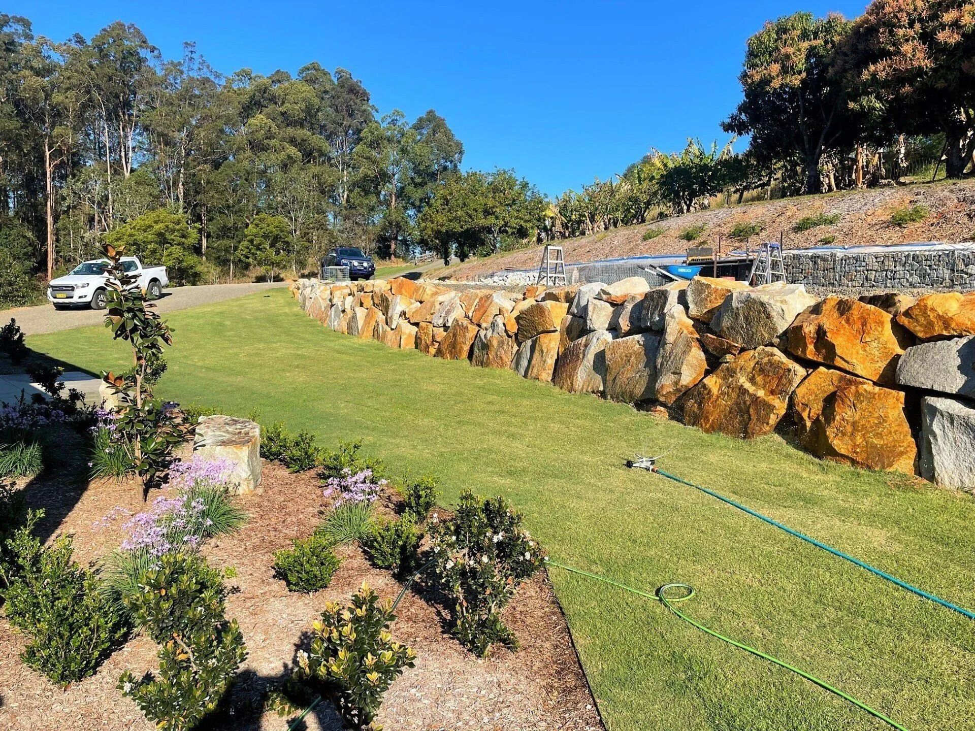 Aa Stone Retaining Wall Along a Grassy Lawn — Blue Dog Earthmoving Landscape Supplies in Newee Creek, NSW