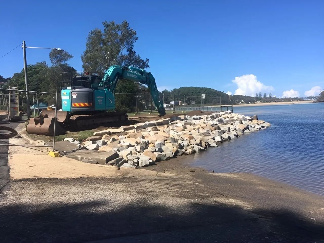 Excavator Placing Large Rocks Along a Shoreline to Build a Retaining Wall — Blue Dog Earthmoving Landscape Supplies in Newee Creek, NSW