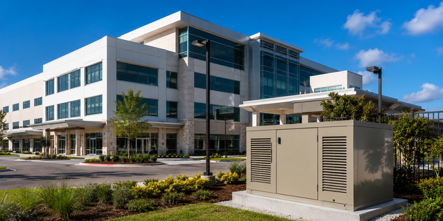 Modern office building with glass windows, parking lot, and utility equipment in the foreground