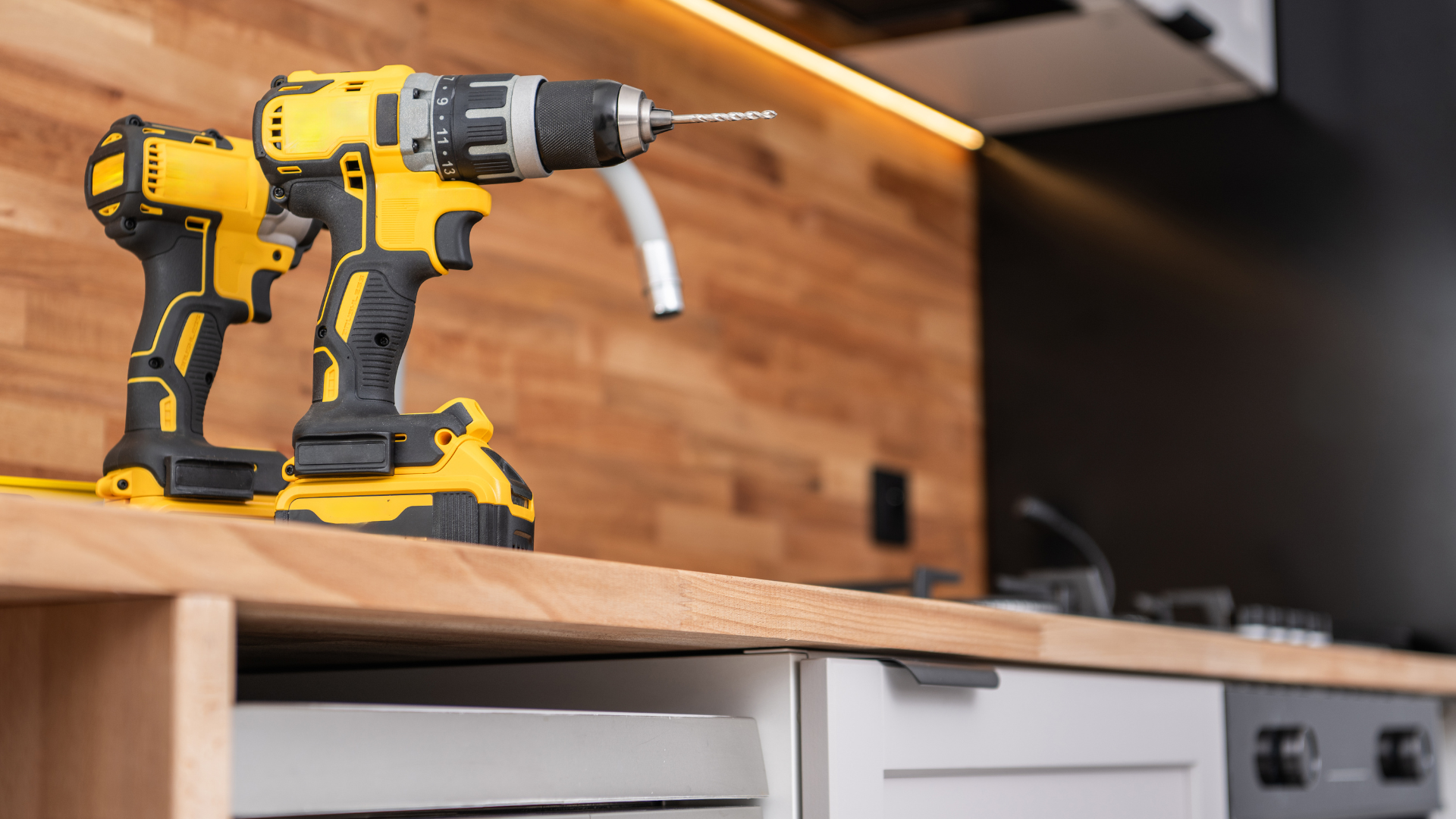 Two drills are sitting on a wooden counter in a kitchen.