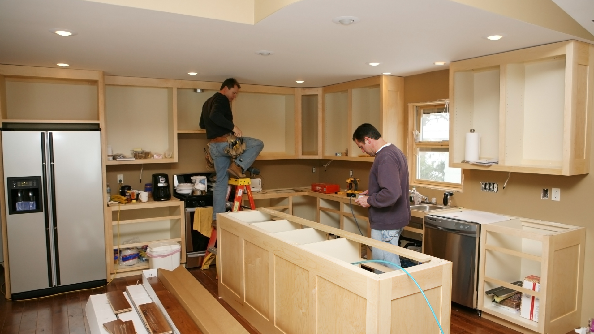Two men are working in a kitchen with a white refrigerator