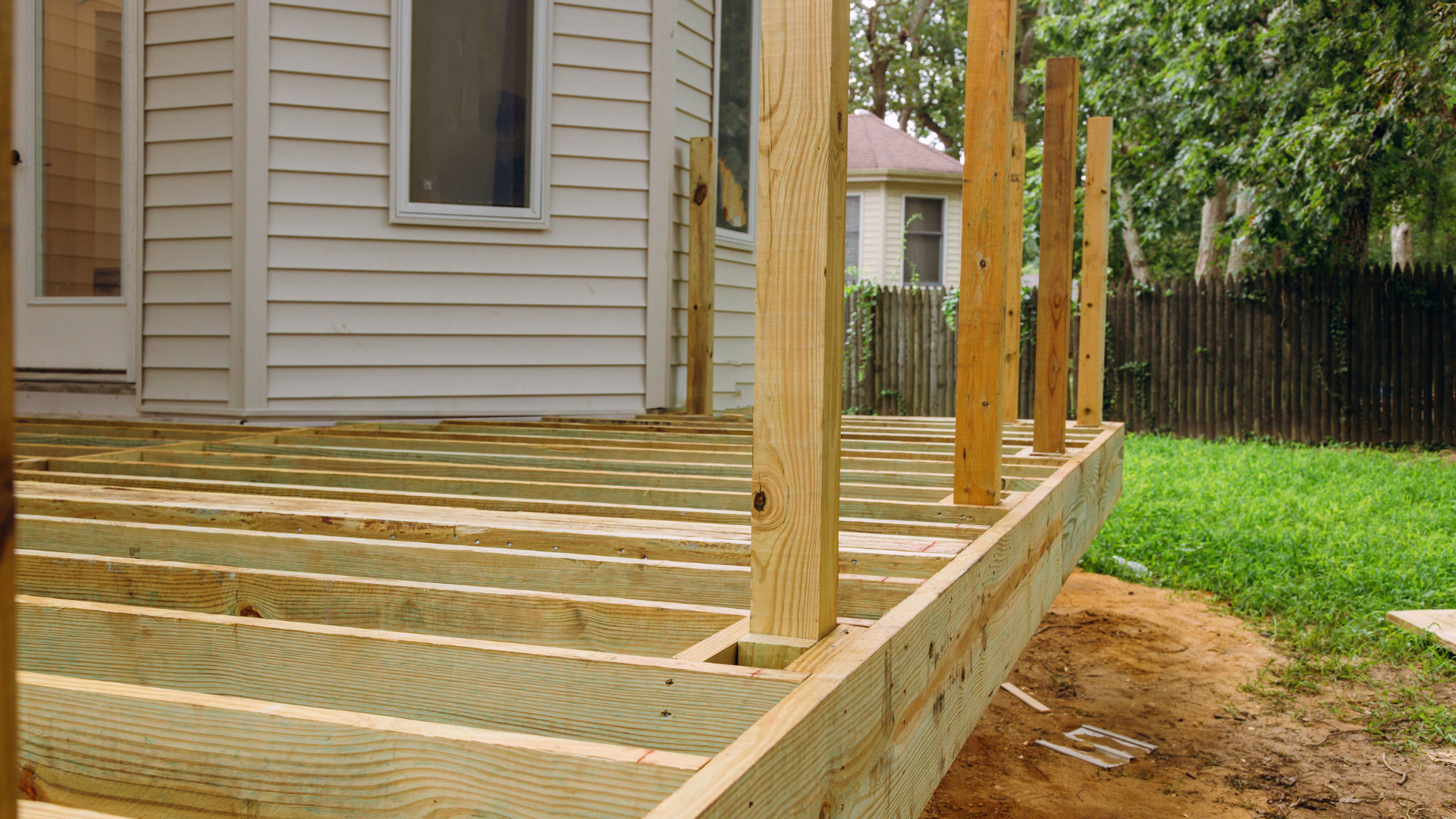 A wooden deck is being built in front of a white house.