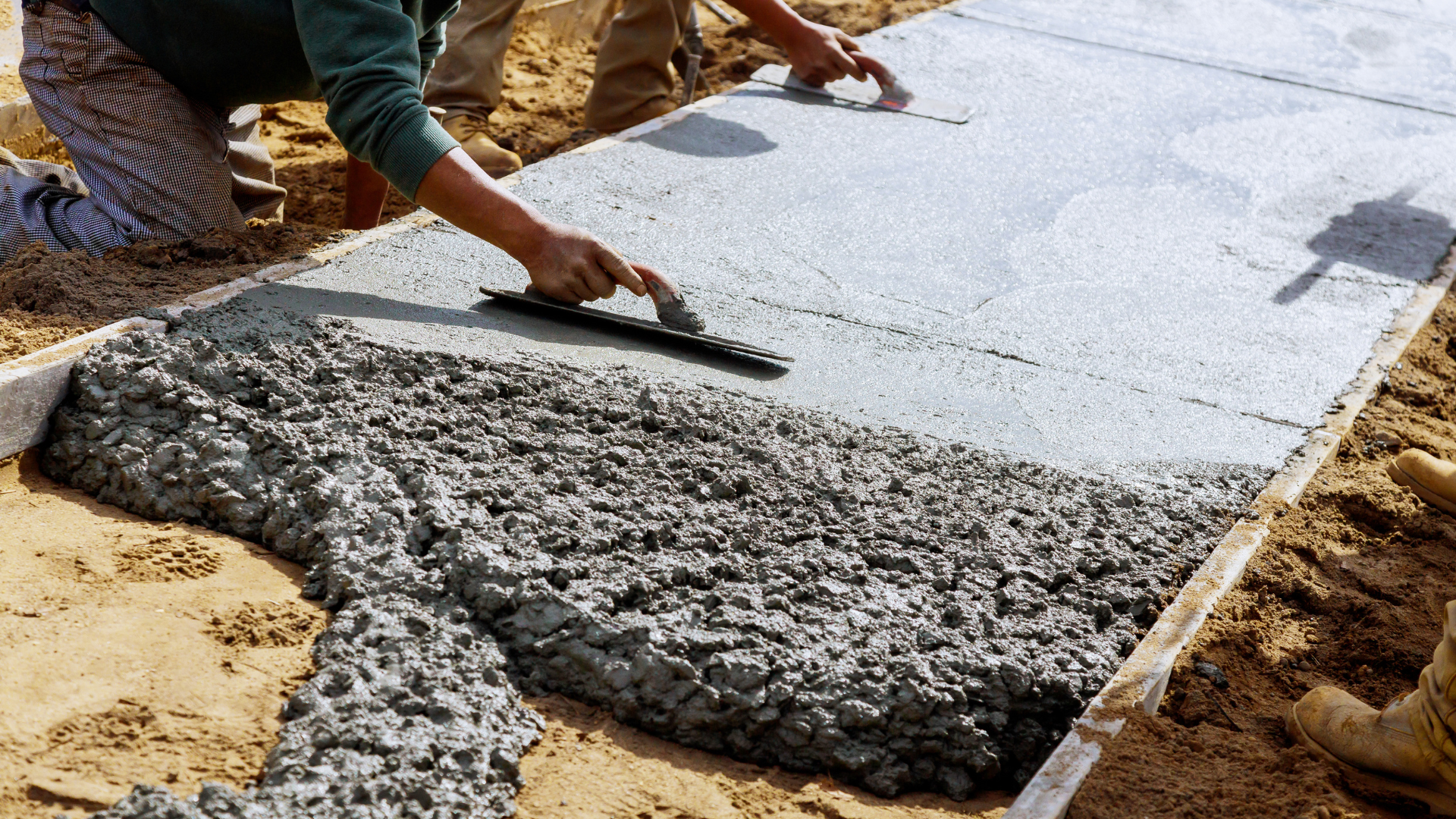 A man is spreading concrete on a sidewalk with a trowel.