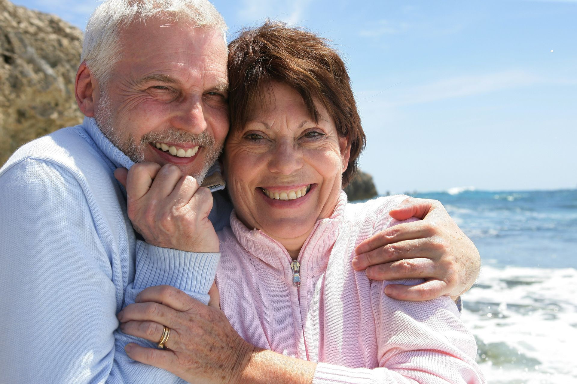 Smiling couple embracing on a sunny beach with ocean waves in the background