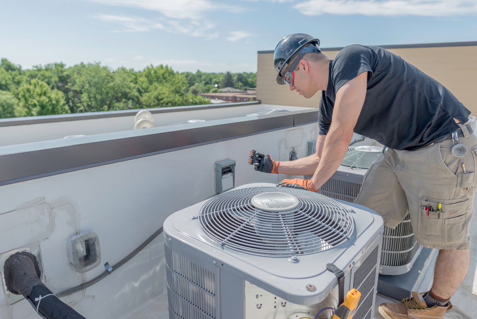 A man is working on an air conditioner on the roof of a building.