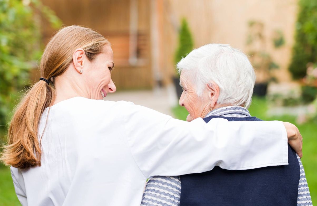 Two people walking arm in arm outdoors, one comforting the other in a garden setting