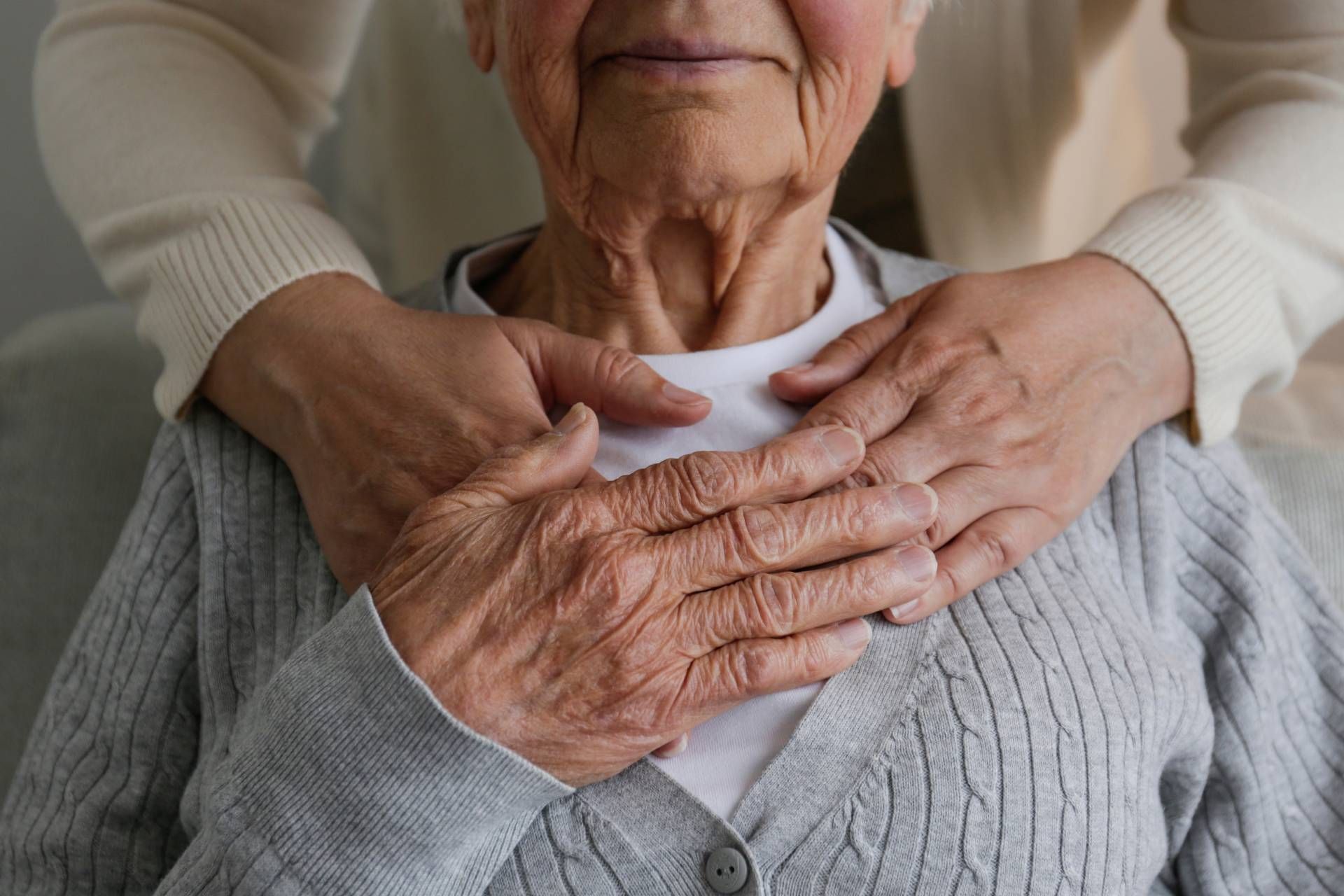 Hands resting on an elderly person’s shoulders and chest in a gentle caregiving gesture