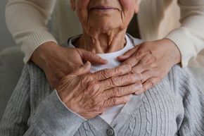 Hands resting on an elderly person’s shoulders and chest in a gentle caregiving gesture