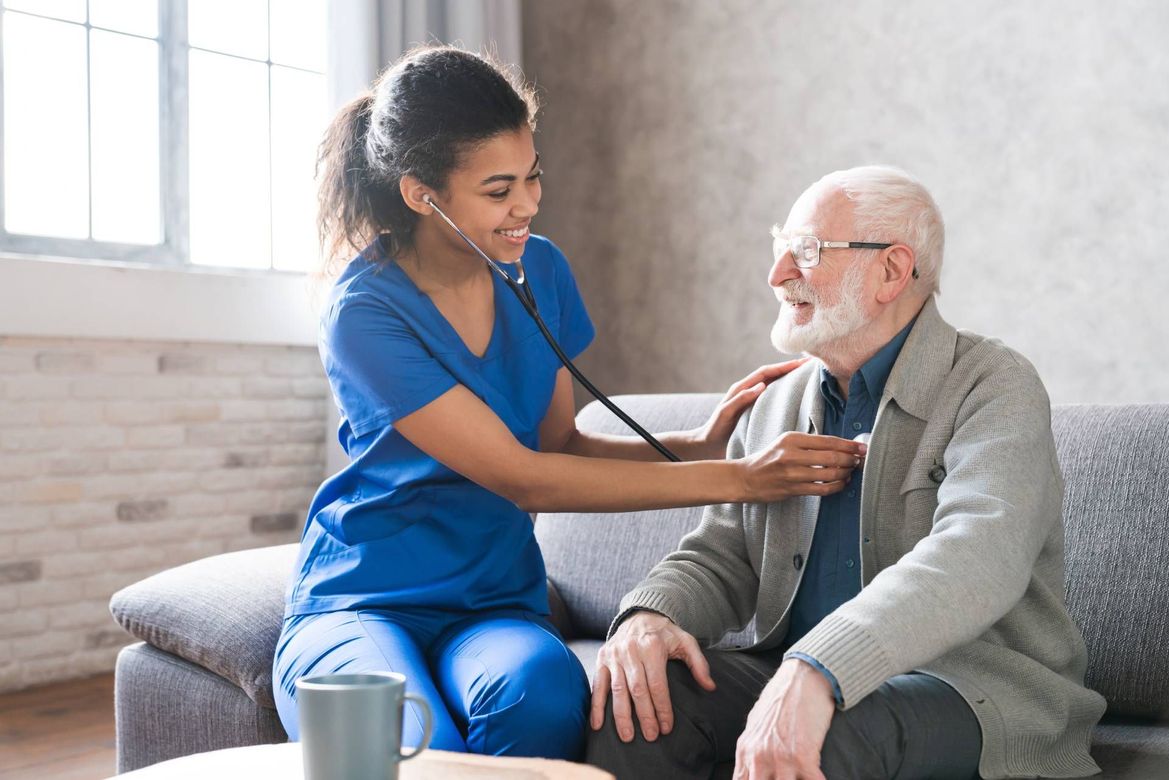 Nurse in blue scrubs checking an older man’s blood pressure in a bright living room