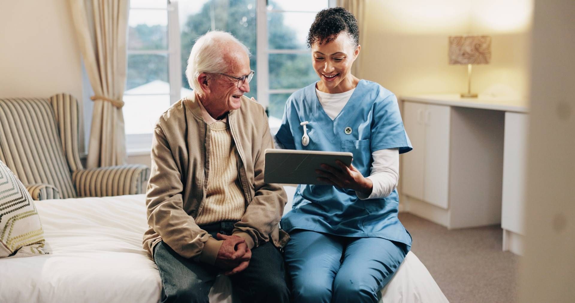 Caregiver showing a tablet to an older adult on a couch in a bright living room