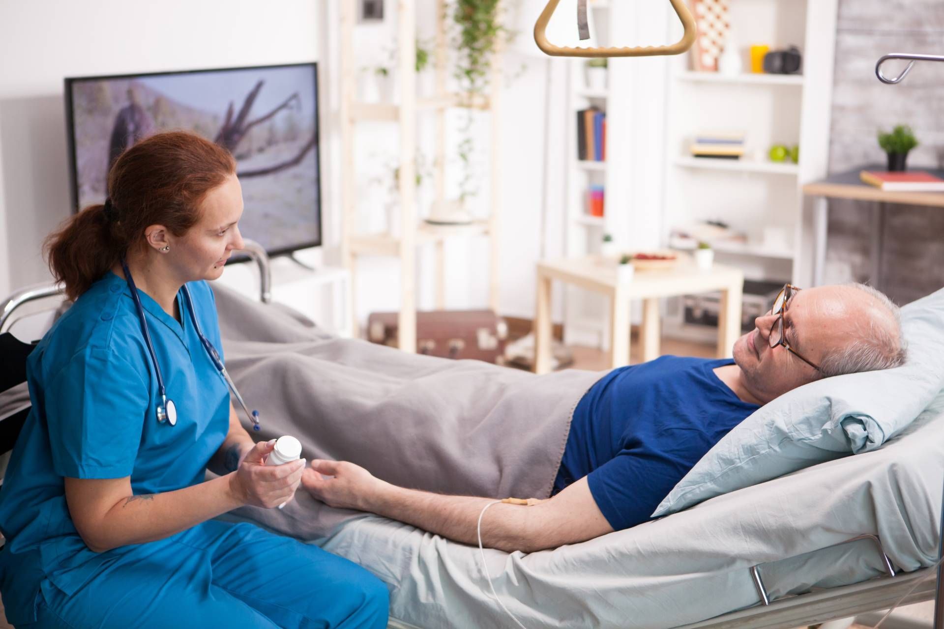 Nurse in blue scrubs holding an elderly patient’s hand in a hospital bed room