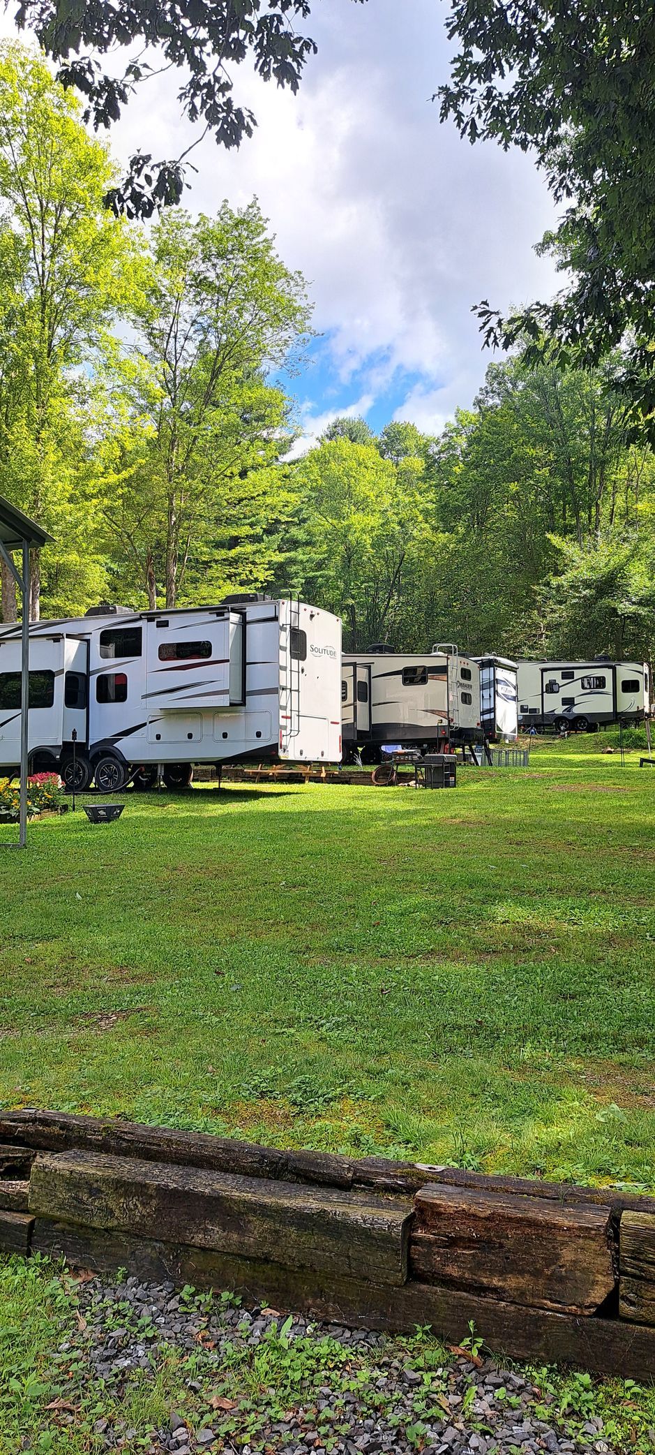 White RVs parked on a grassy hillside beside trees under a cloudy sky