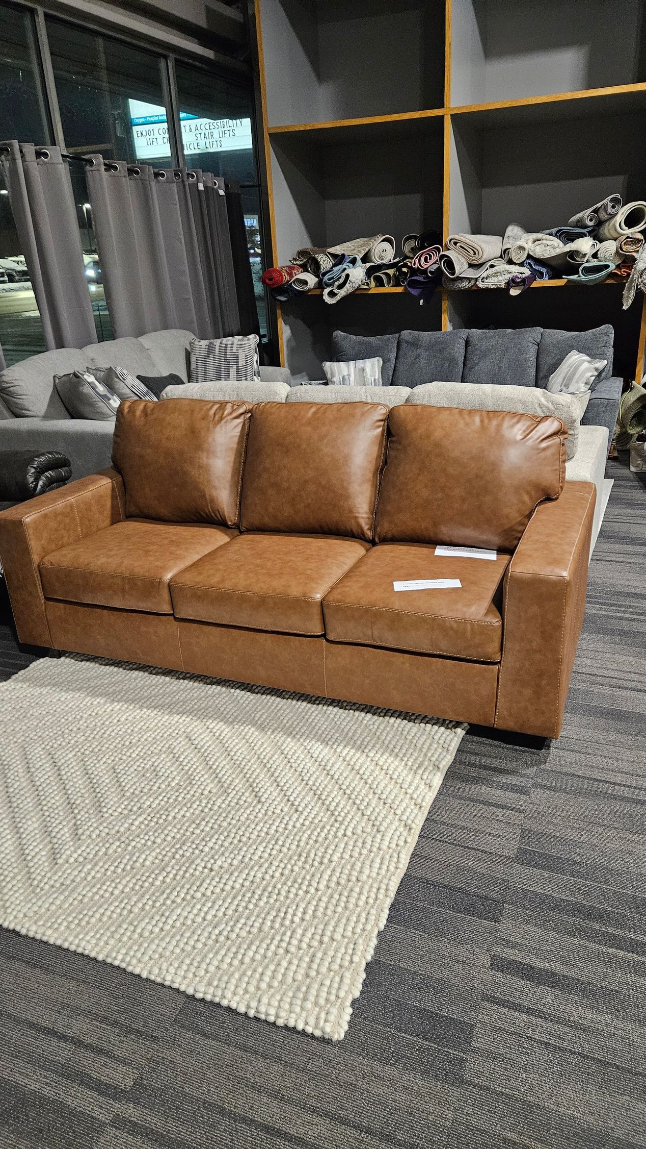 Brown leather sofa with three cushions on a white rug in a furniture store.