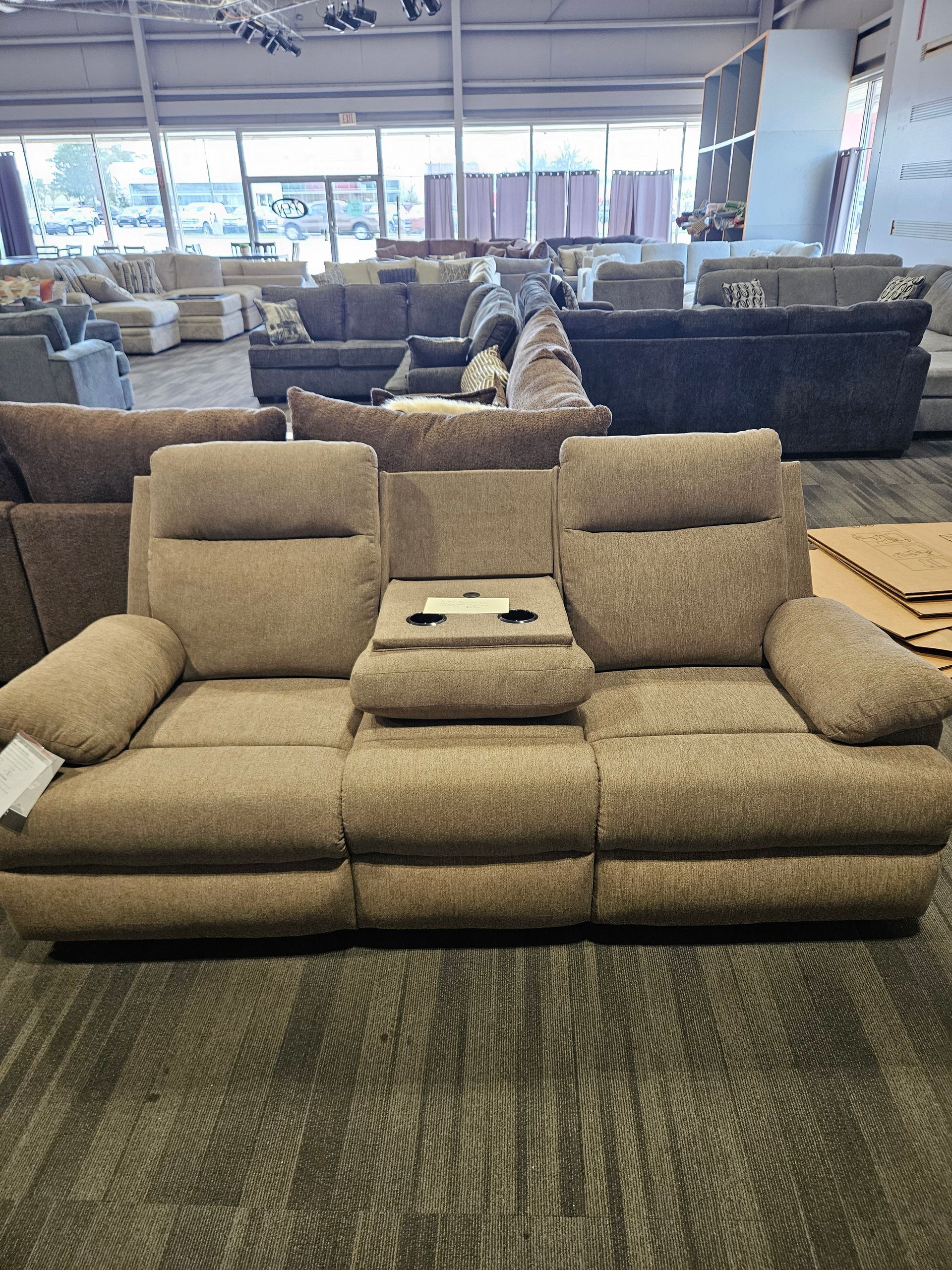 Tan reclining sofa with a center console containing cup holders, in a furniture store.