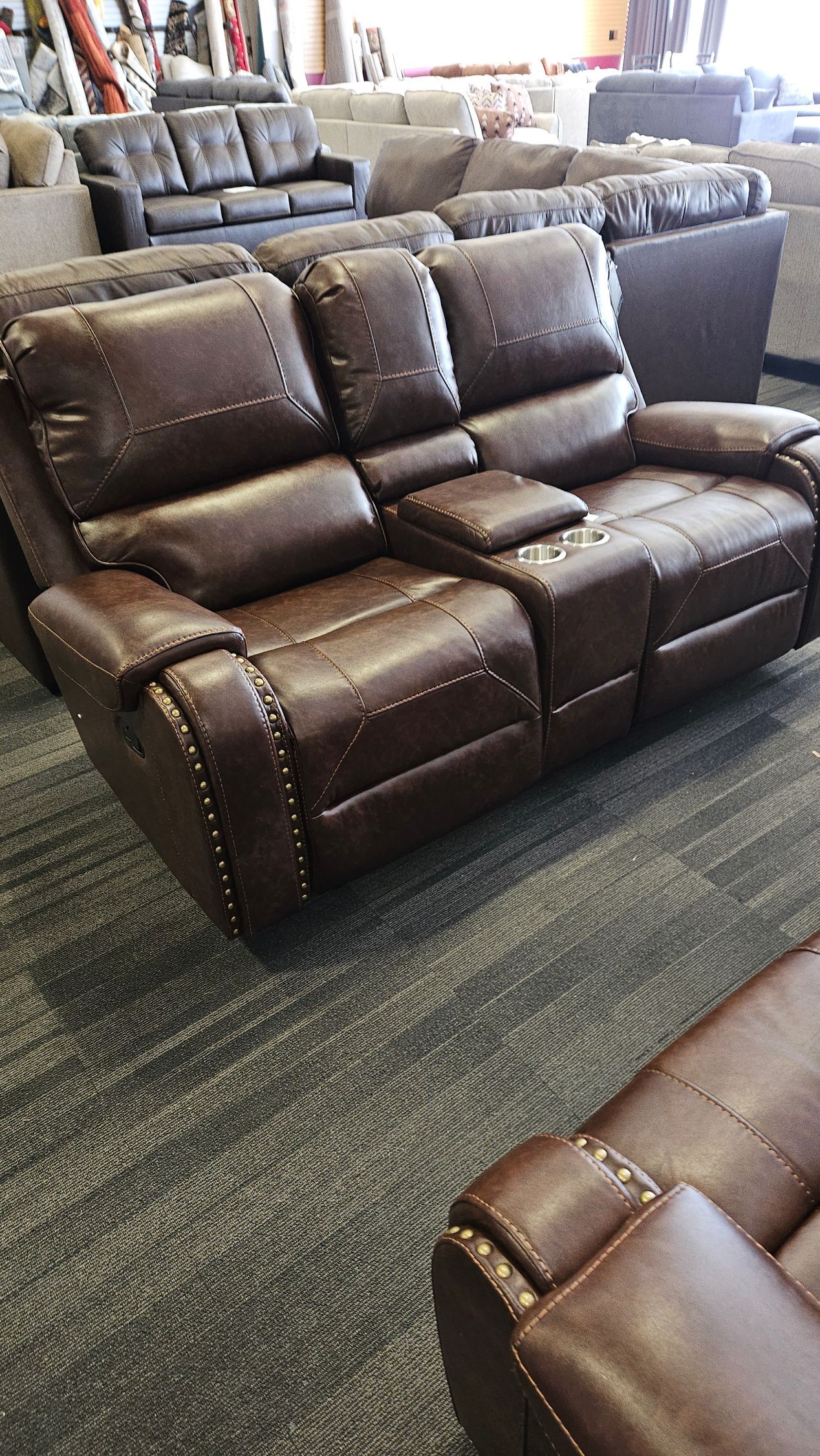 Brown leather recliner sofa with cup holders and studded details in a furniture store.