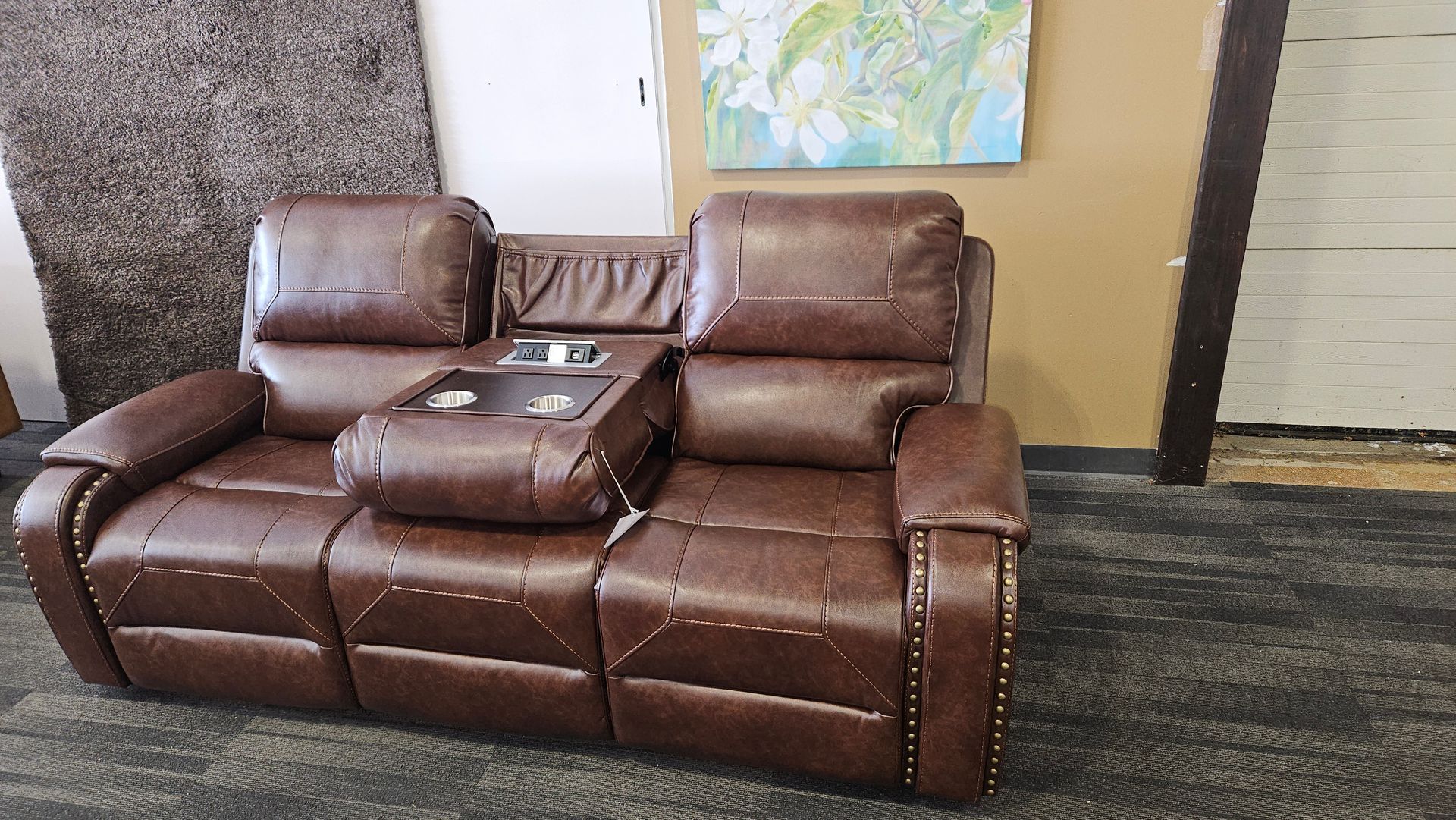 Brown leather reclining sofa with center console, on a patterned rug.