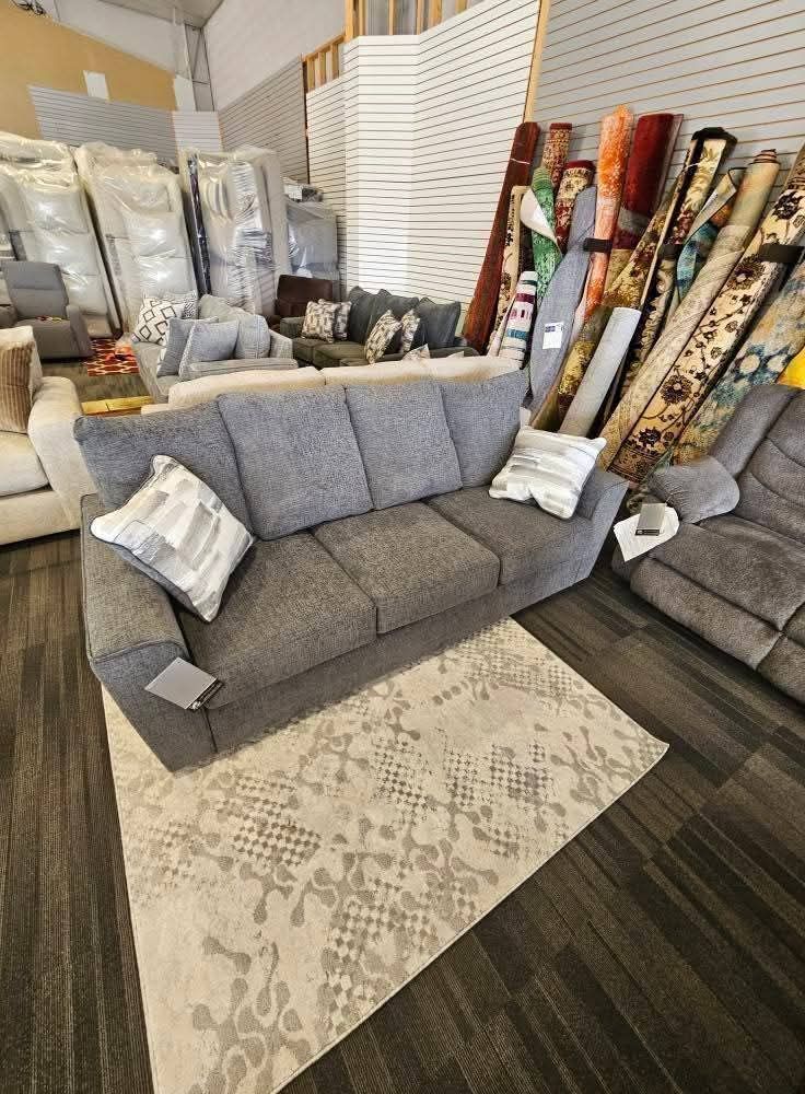Gray sofa with patterned rug in a furniture store. Rugs and other furniture in background.