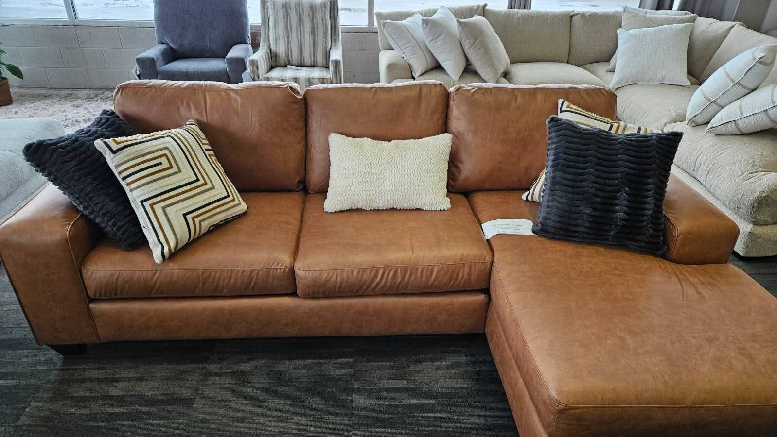 Brown leather sectional sofa with pillows in a furniture store.