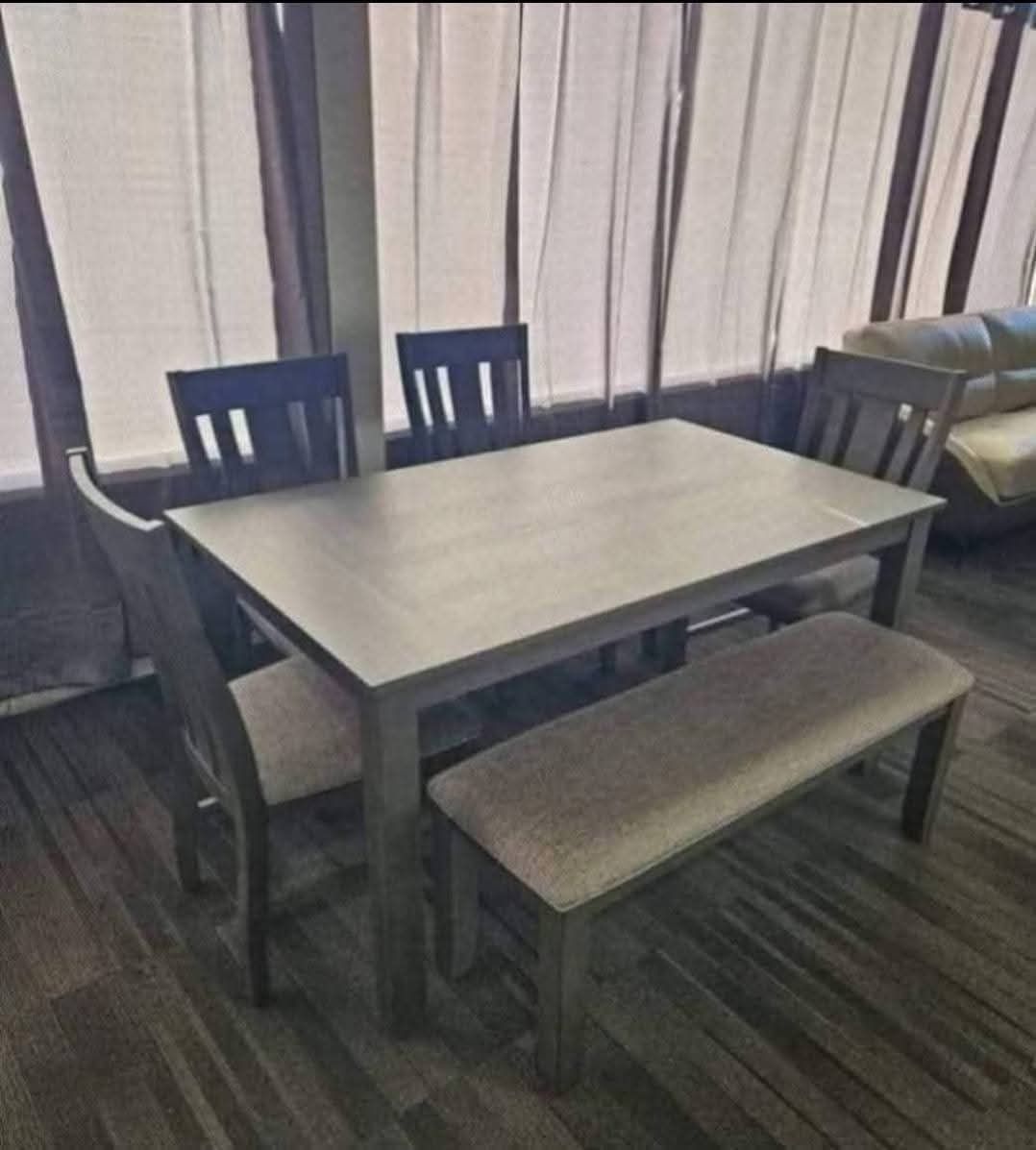 Dining table set with four chairs and a bench, all gray. Beige upholstered bench seat.