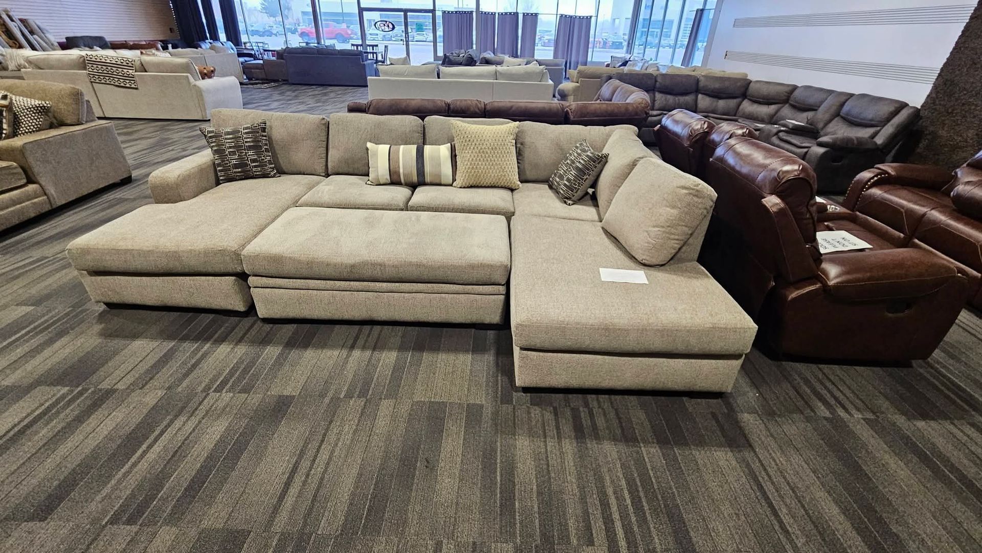 Beige sectional sofa in a furniture store showroom with other furniture in the background.