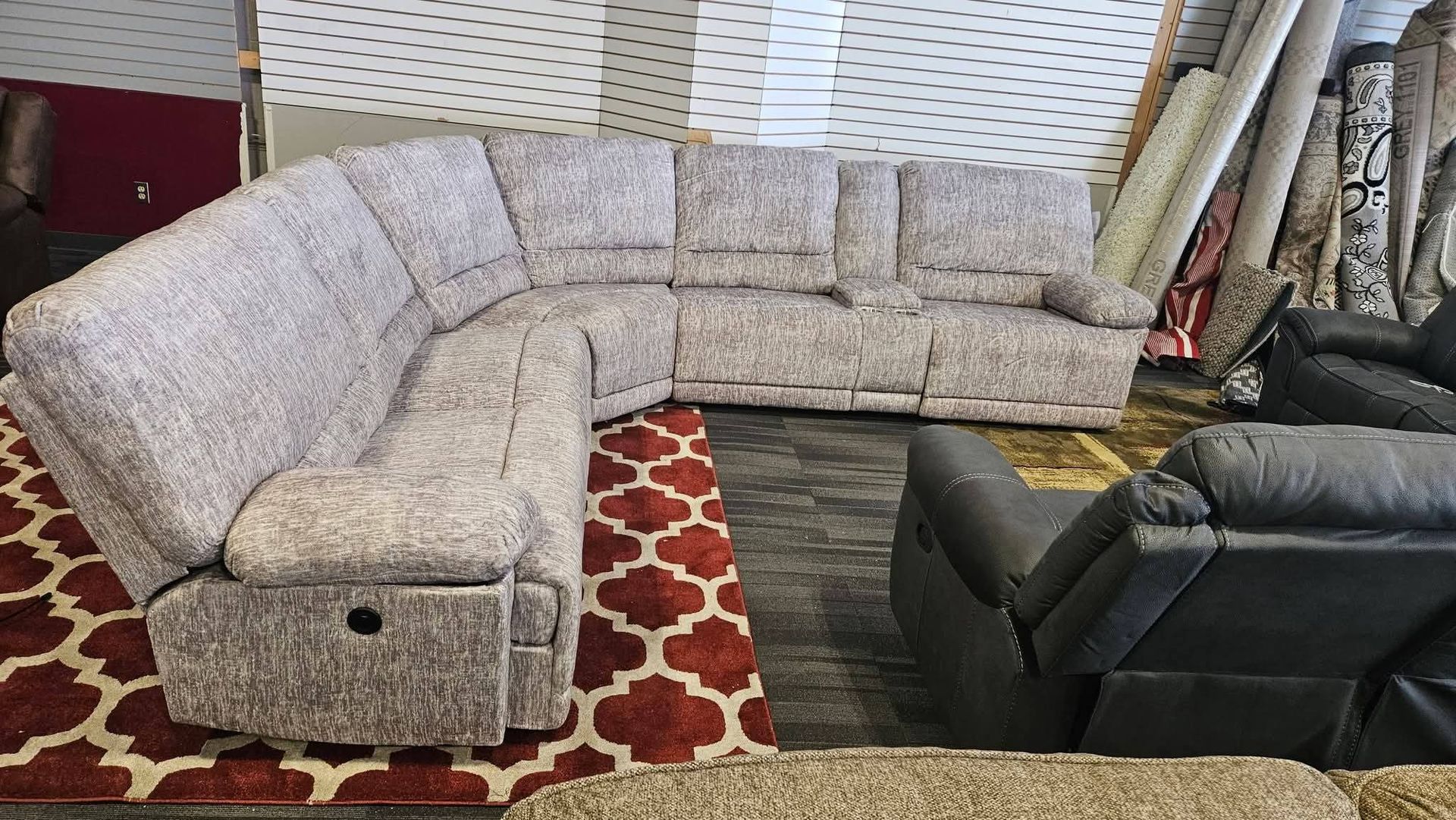 Beige sectional sofa in a furniture store, red rug below, and black recliner chair.
