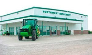 Green John Deere tractor parked in front of Northwest Implement dealership, green and white building.