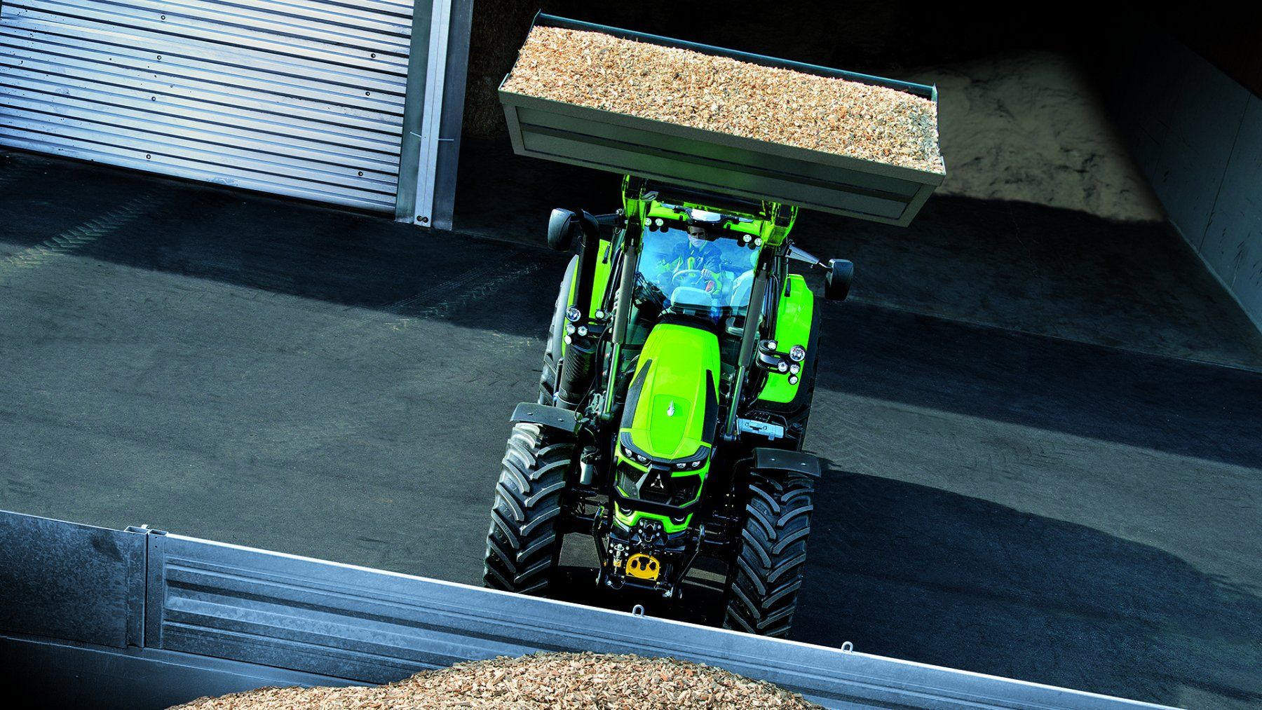 Green tractor with a full front bucket of material, at a storage area.