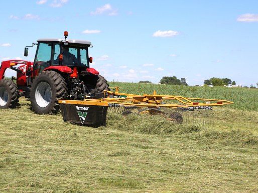 Red tractor with attached hay rake in a field on a sunny day.