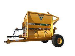 Yellow Vermeer SPX9010 hay mixer. Farm machinery with large tires, angled chute, and tow arm.