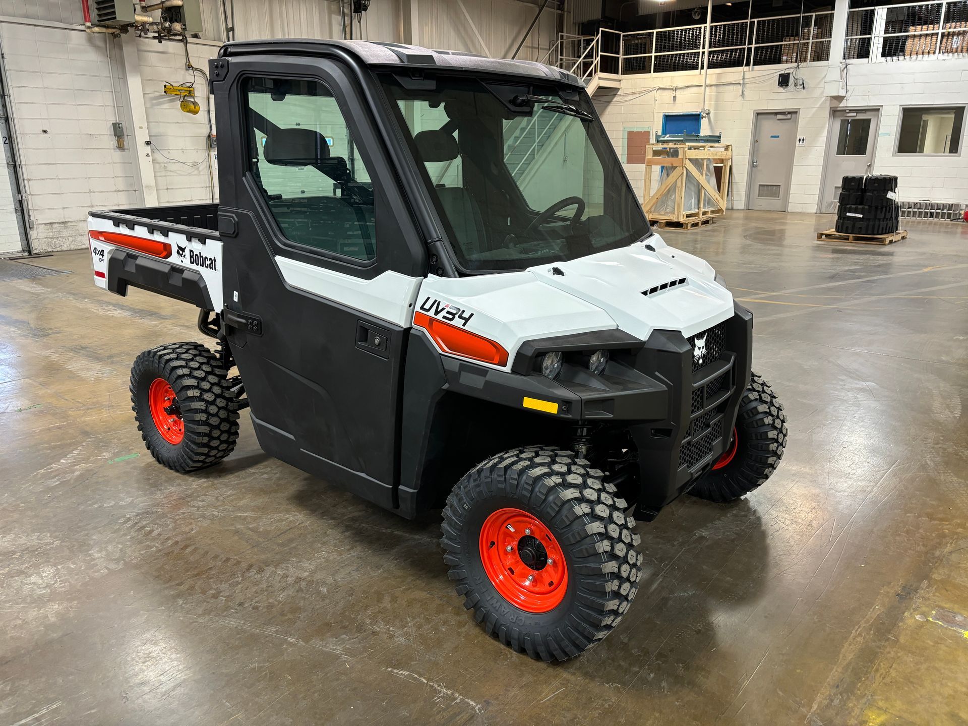 White and black Bobcat utility vehicle with red wheels and a cabin, in a warehouse setting.