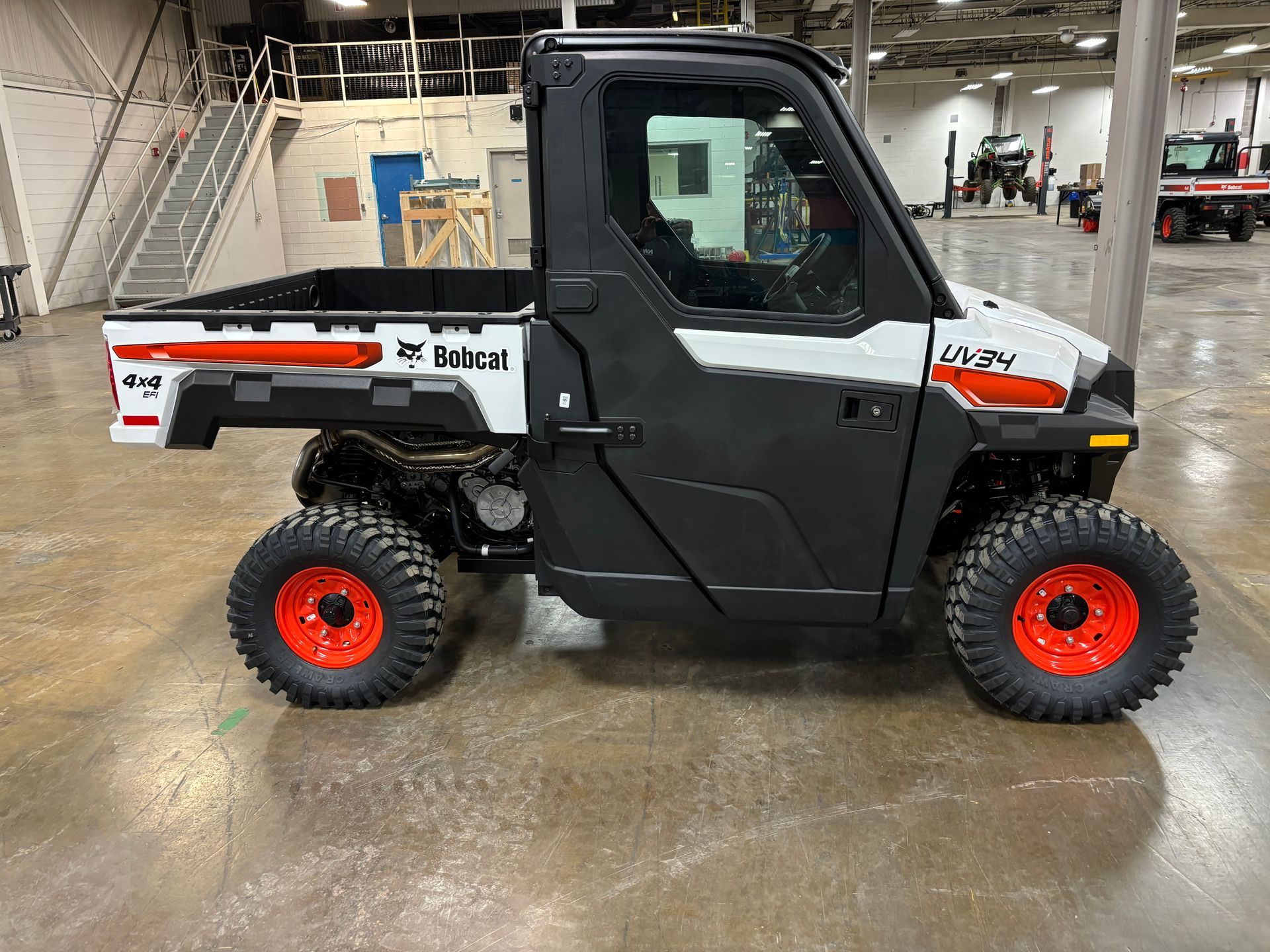 Bobcat UTV with enclosed cabin, black and white, orange wheels, indoors.