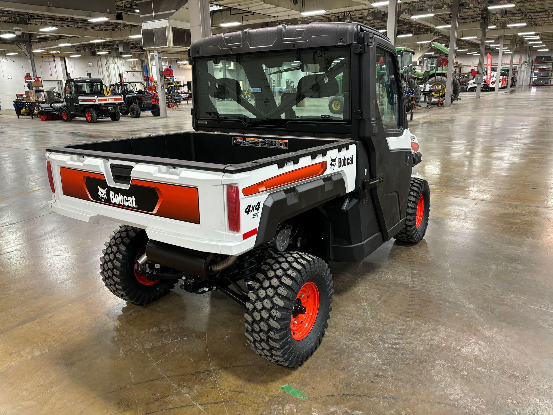 Bobcat utility vehicle with black cab and orange wheels, parked inside.