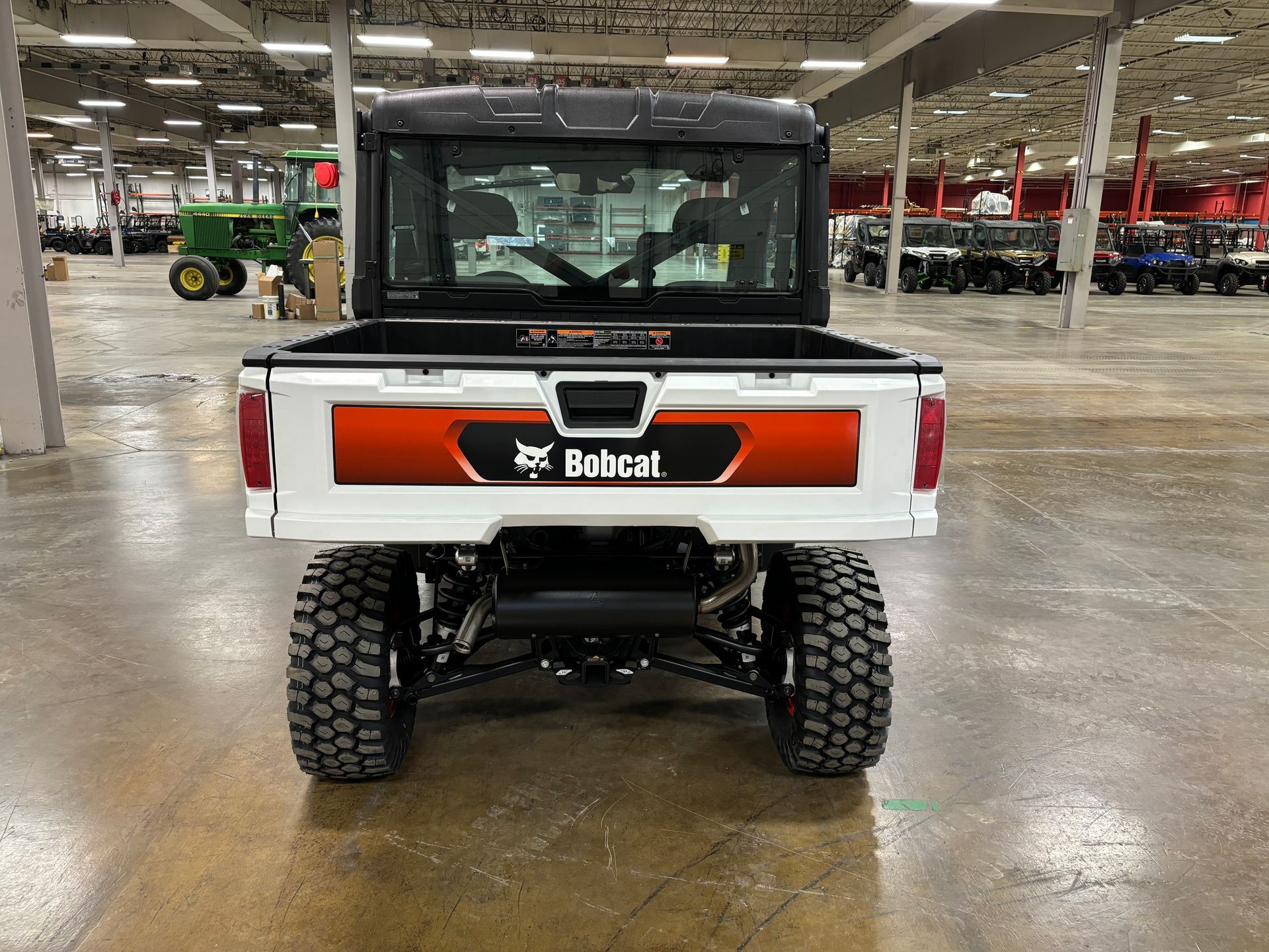 White Bobcat utility vehicle with orange accents, large tires, and a black cab, viewed from the rear.